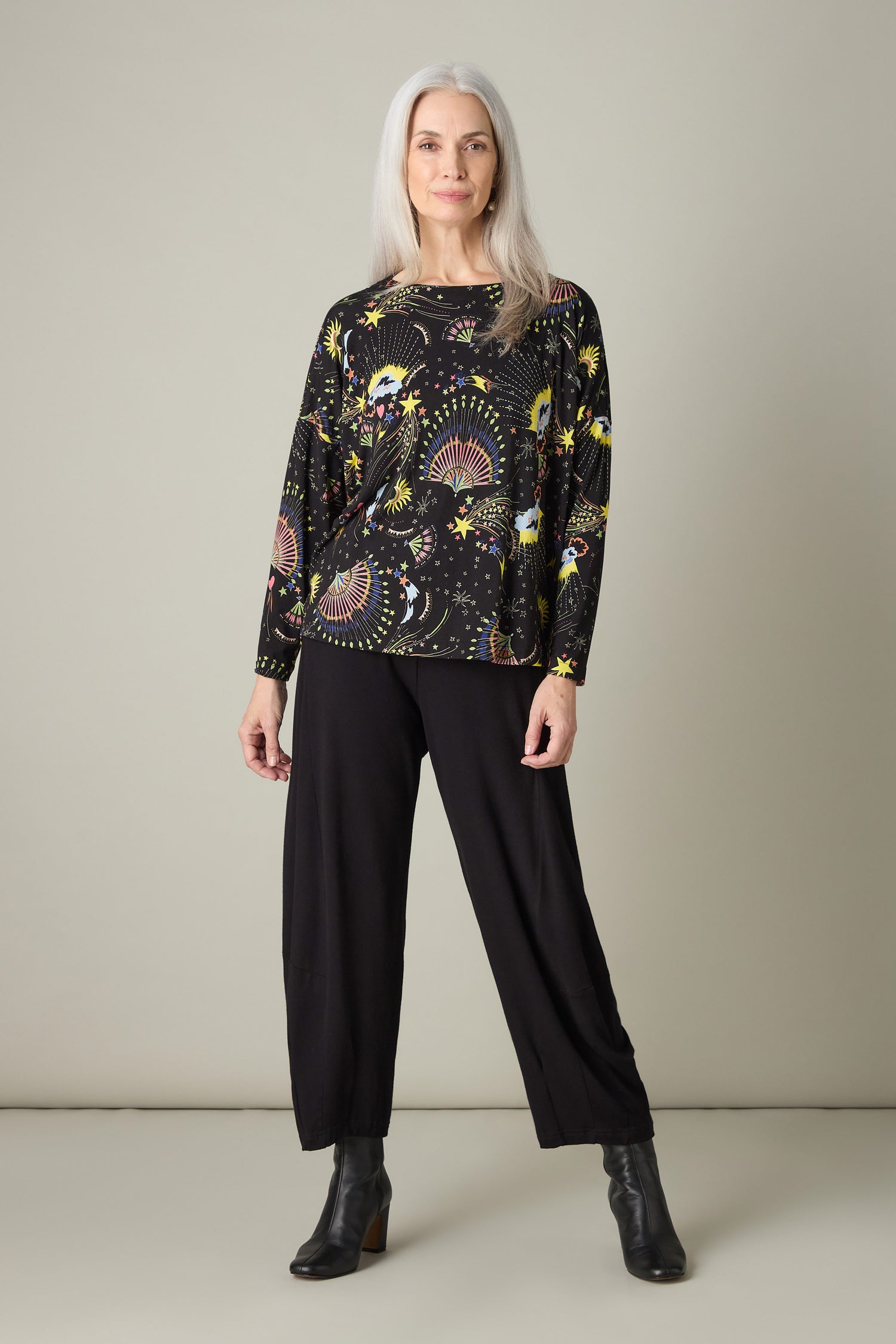 A woman with long gray hair is wearing the Celestial Dreams Jersey Boxy Top and black pants as she stands against a plain background.