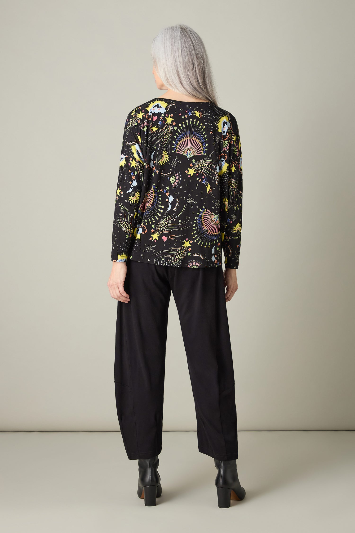 A person with long gray hair is wearing a Celestial Dreams Jersey Boxy Top and black pants, standing against a plain background.