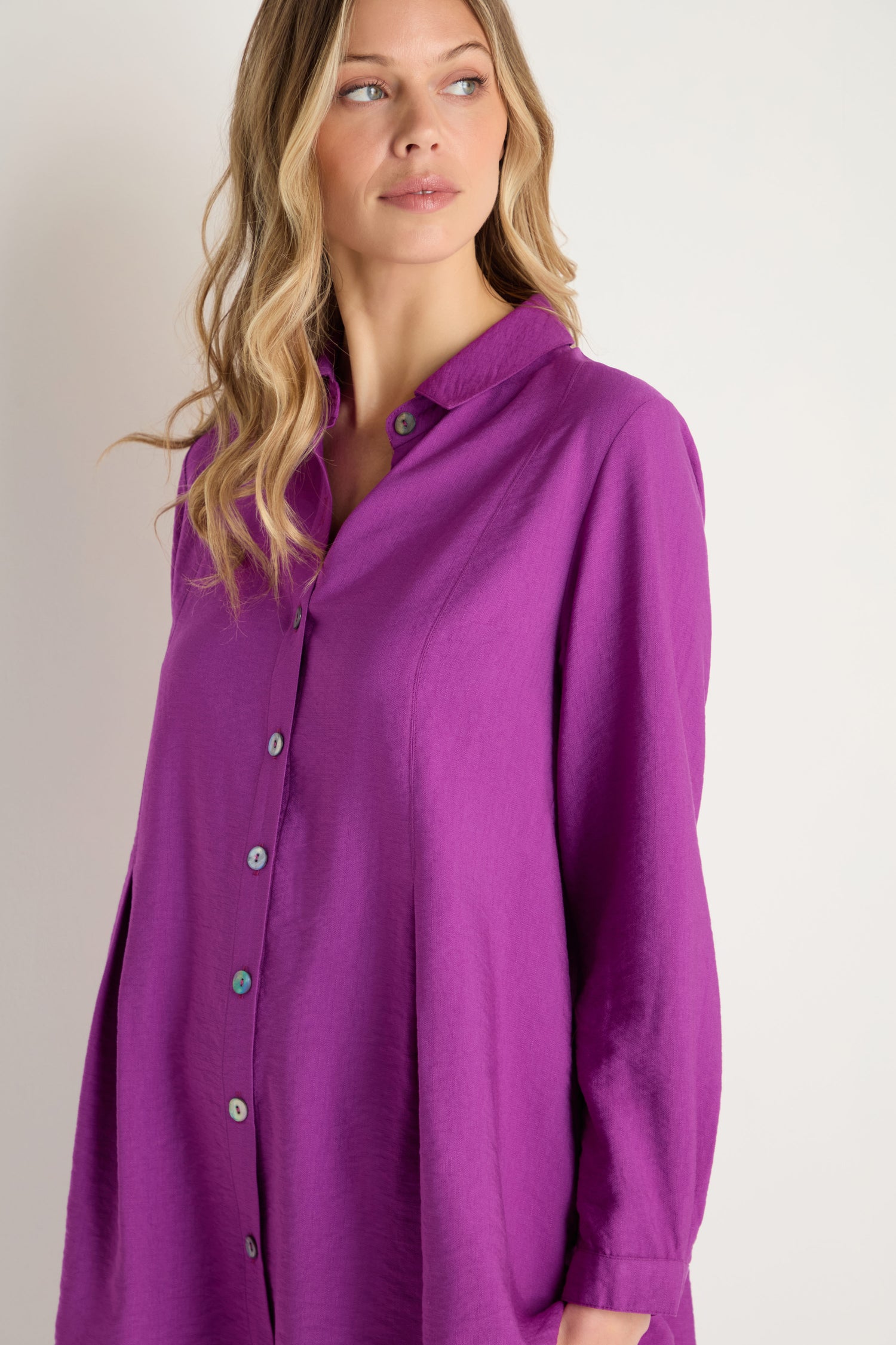 A woman with wavy blonde hair looks to the side, wearing the Textured Viscose Pleat Shirt in purple—a loose-fitting, long-sleeve style.