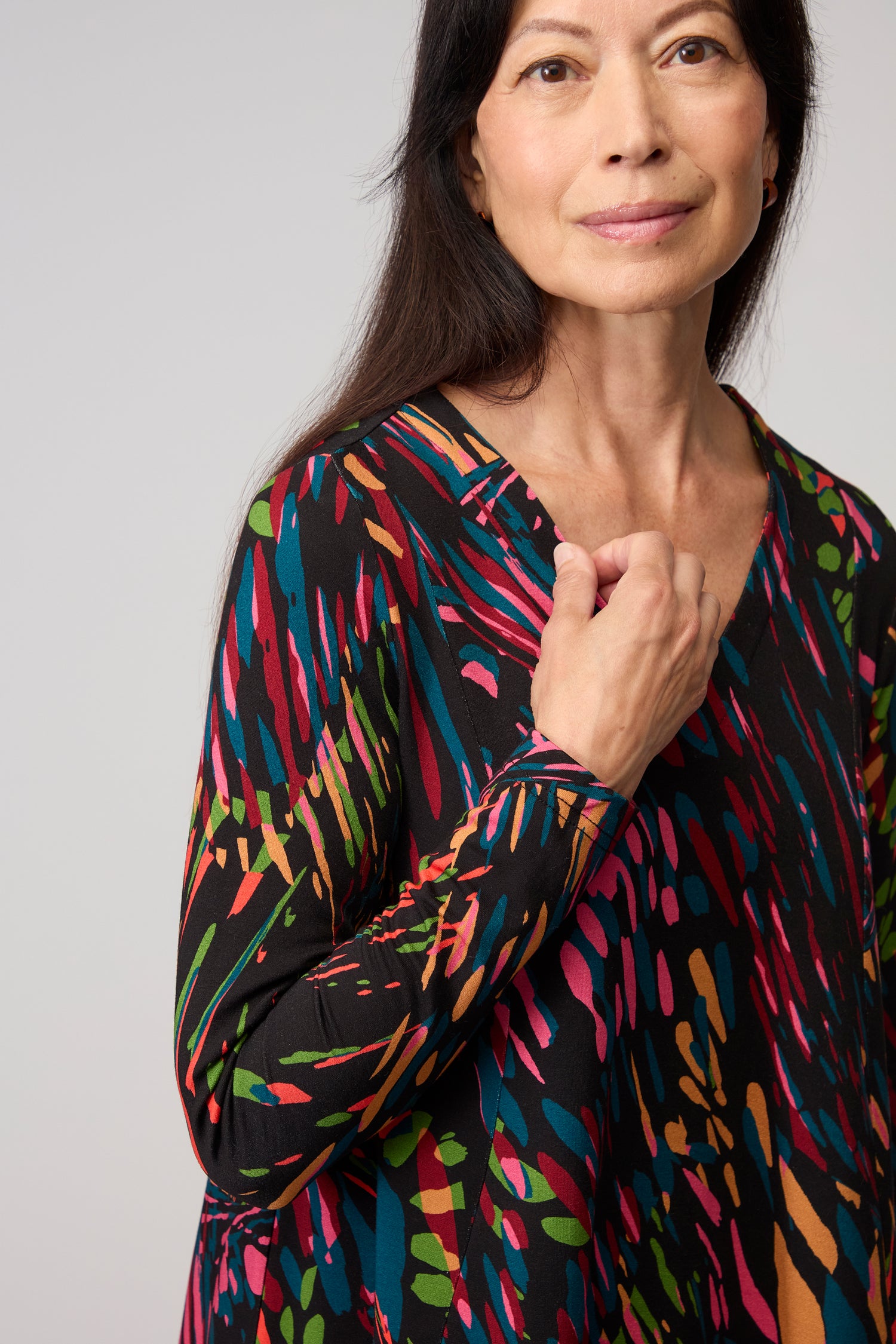 A woman with long dark hair wears the Skyfire Jersey Top, an abstract print piece made from Lenzing EcoVero jersey, standing against a light background and looking at the camera with a neutral expression.