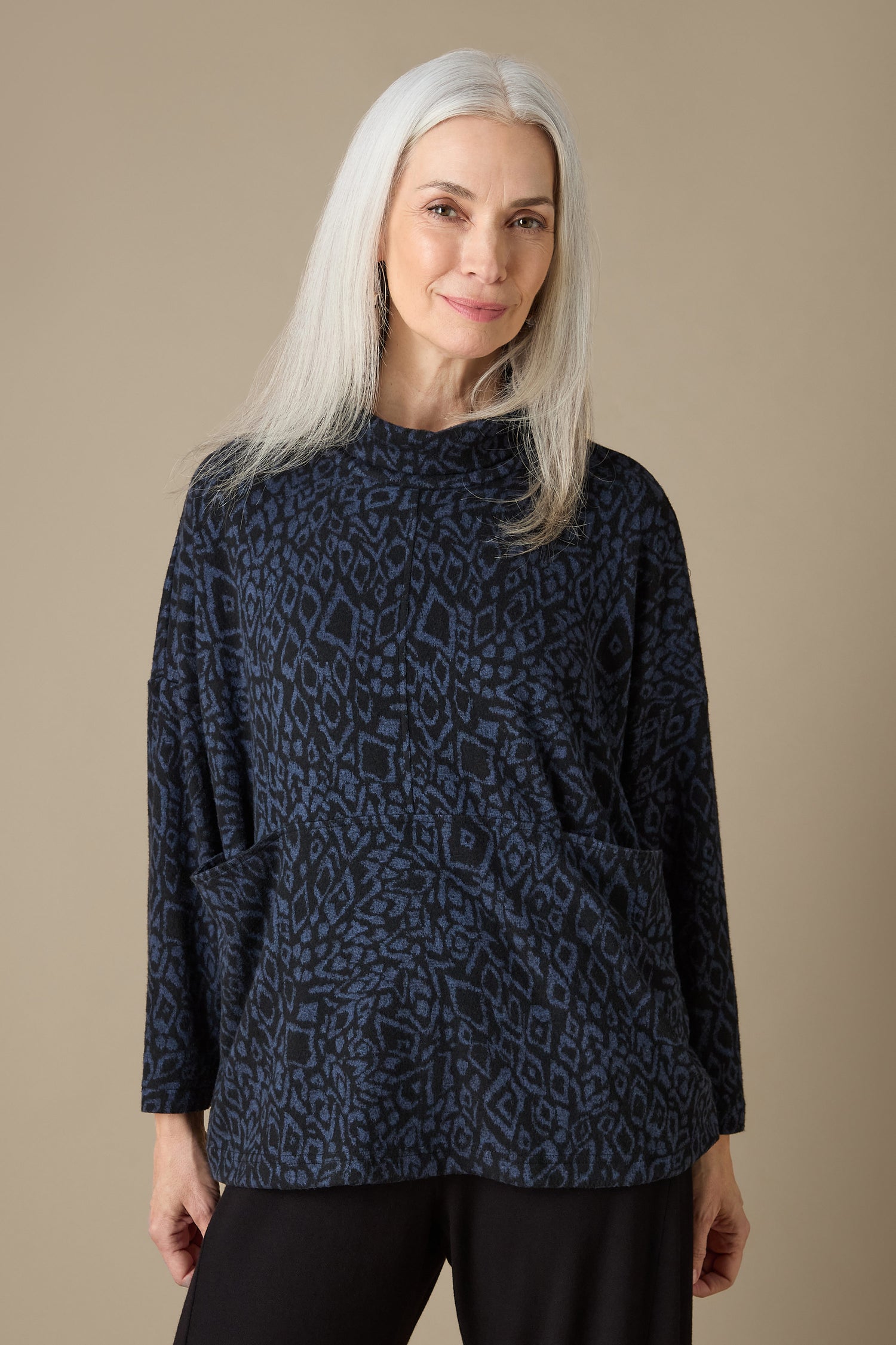 A woman with long white hair wears an Ikat Soft Jersey Relaxed Top, showcasing a patterned dark design, while standing against a plain background.
