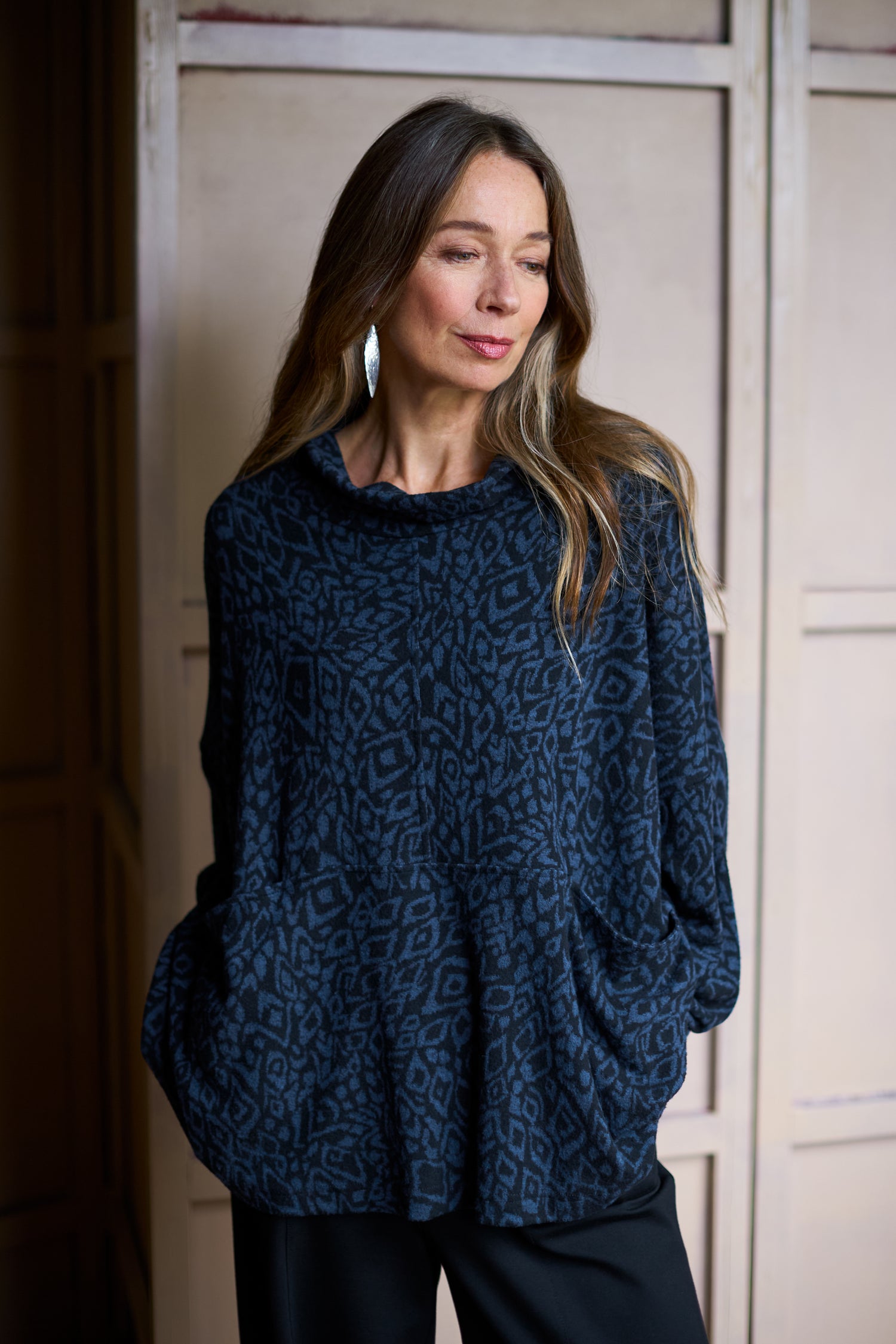 A woman stands with a relaxed silhouette, wearing an Ikat Soft Jersey Relaxed Top in a dark blue pattern and wide silver earrings, set against a neutral background.