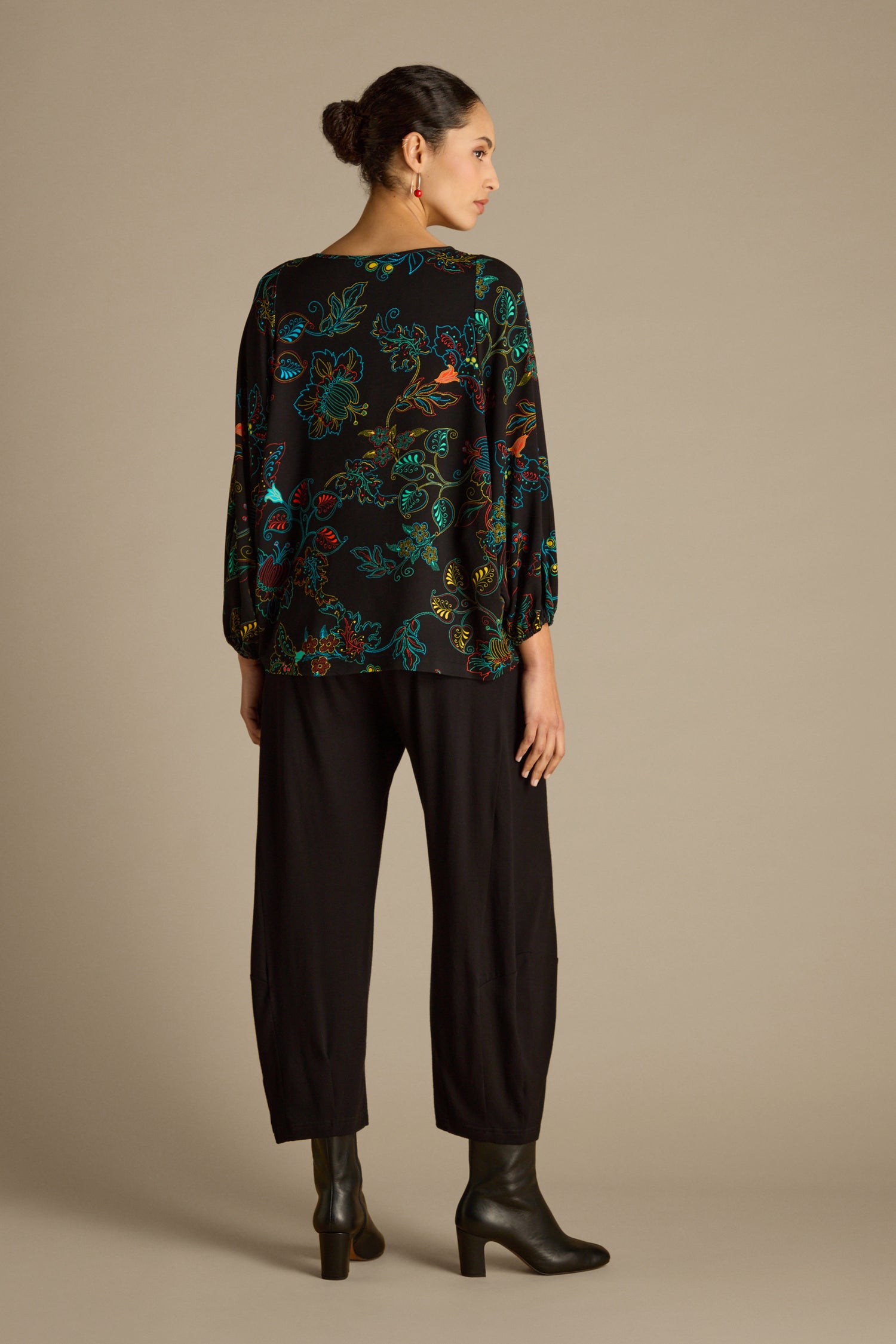A person is seen from behind, dressed in the Bright Dotted Floral Jersey Top paired with black pants and matching boots. The plain beige background adds a simple yet striking contrast.