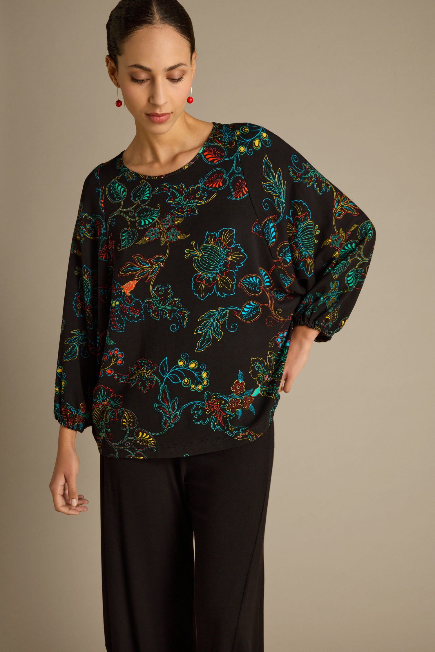 A person wearing an oversized Bright Dotted Floral Jersey Top and black pants stands against a neutral background, looking down with one hand on their hip.