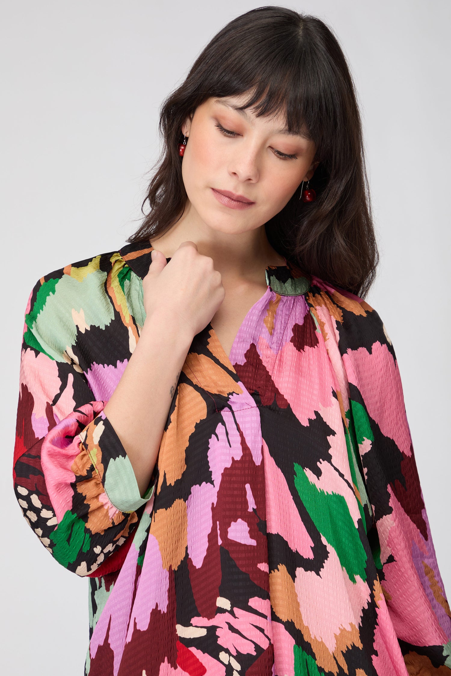A woman poses with one hand on her hip against a neutral background, wearing the Floral Collage Print Top featuring rolled sleeves, a relaxed silhouette, and a vibrant floral collage print.