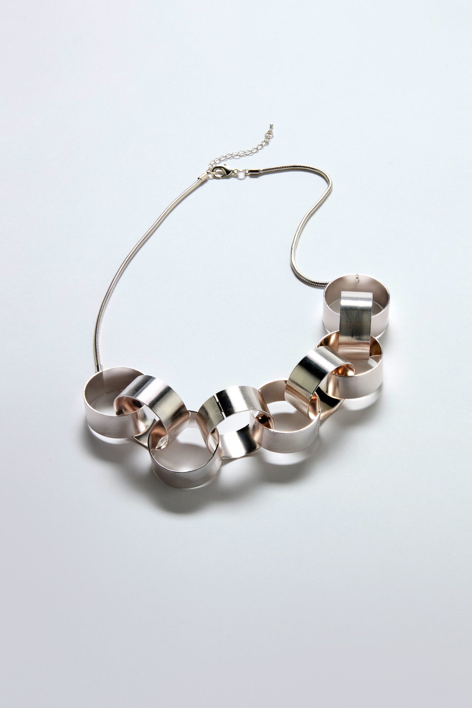 The Affinity Hoop Necklace features large interlocking circles in a brushed silver finish and a slim, adjustable chain, showcased against a light background.