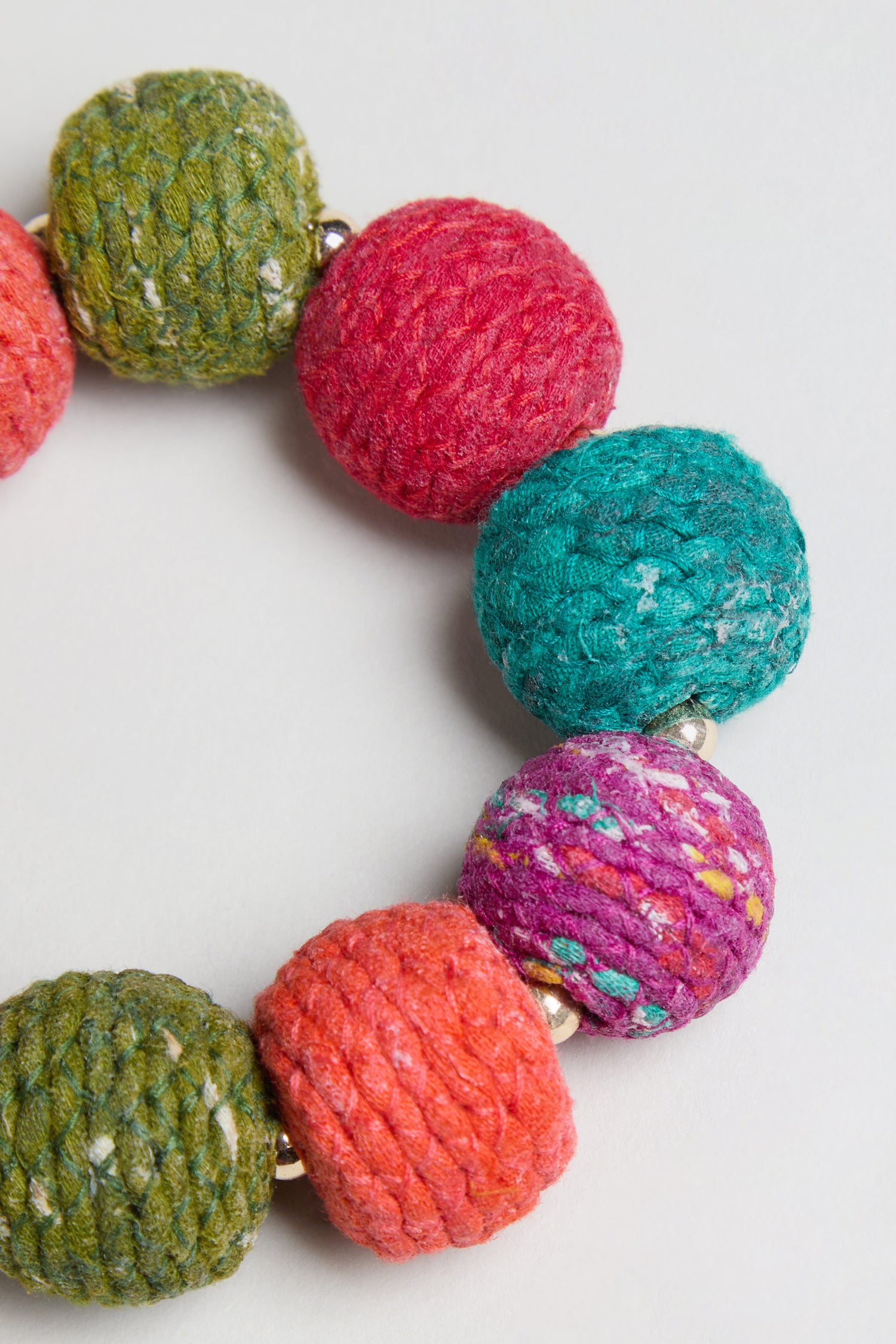 Close-up of the Rainbow Kantha Spheres Bracelet, which features large, cotton-wrapped wooden beads in green, red, teal, orange, and purple against a white background. This statement piece highlights vibrant colors and textured details for a bold look.