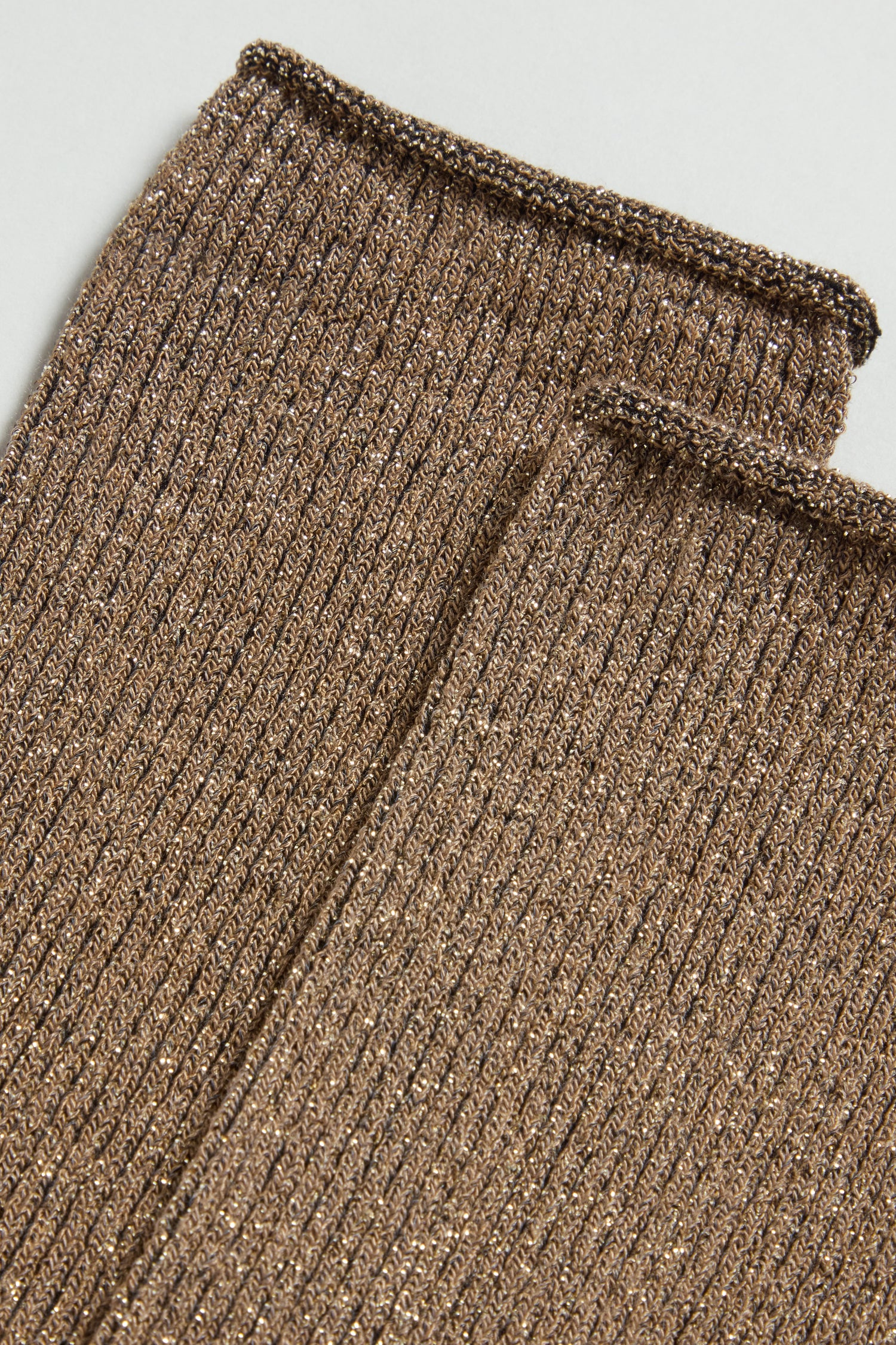 Close-up of two ribbed, metallic gold knit sleeves on a flat surface, capturing the shimmering texture of Bamboo Sparkle Caramel Socks.