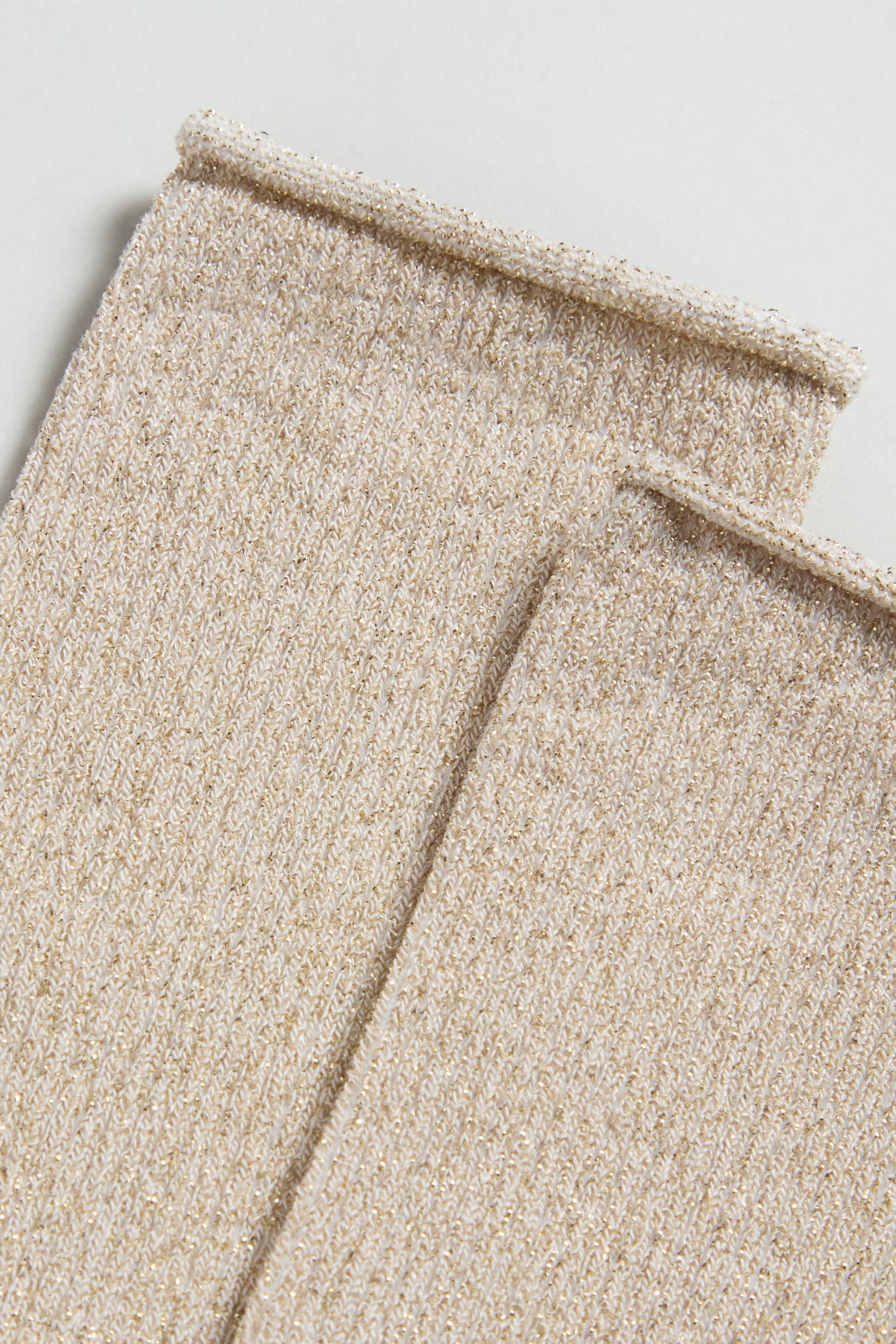 Close-up of the edges of two beige, ribbed knit fabric pieces from Bamboo Sparkle Sand Socks—ideal for crafting eco-friendly socks—laid side by side on a light surface.