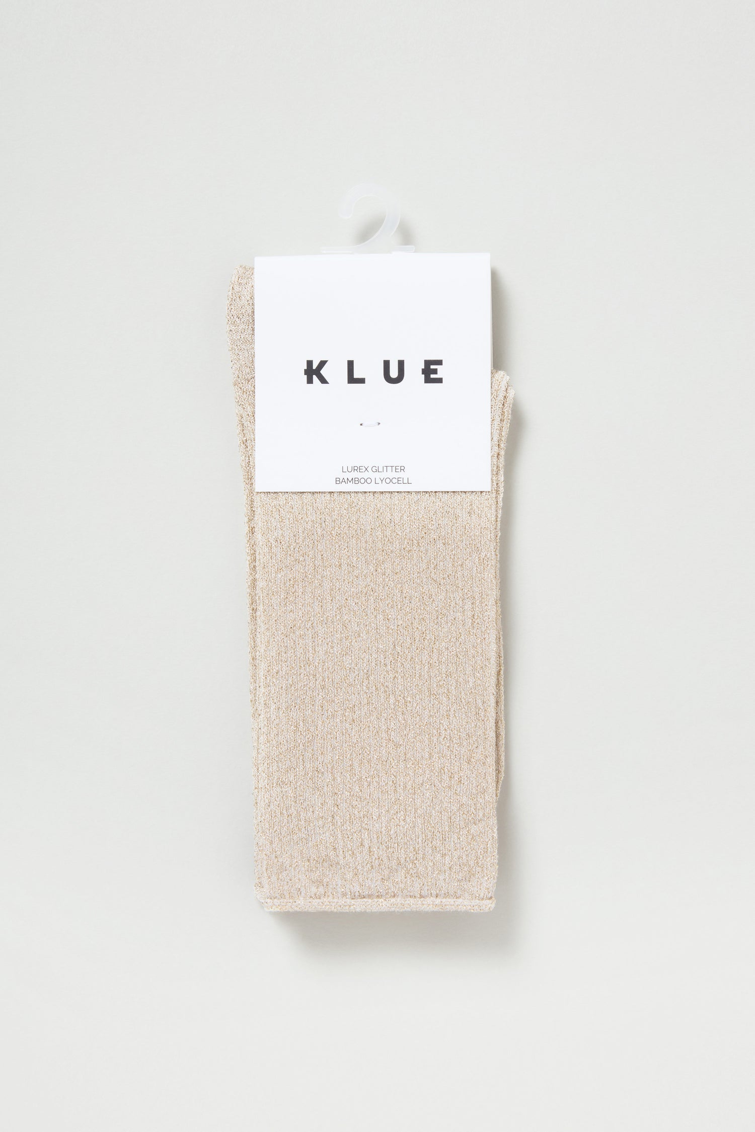 The Bamboo Sparkle Sand Socks are beige glitter socks with a subtle shimmer, crafted from eco-friendly bamboo fibers and packaged with a white label displaying the "KLUE" brand name.