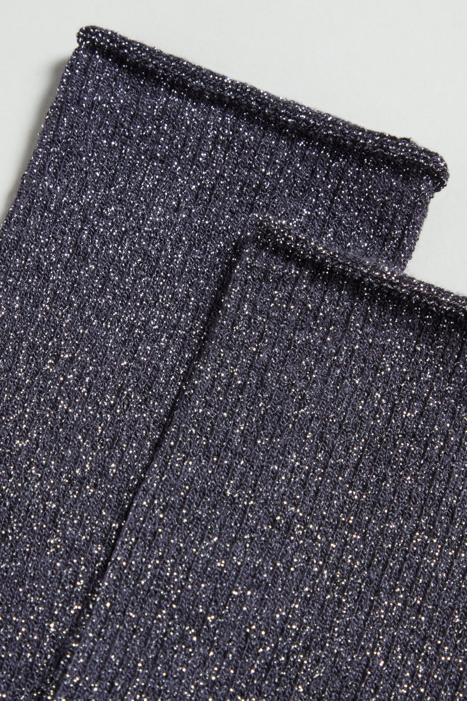 Close-up of Bamboo Sparkle Dark Grey Socks: two pieces of ribbed, dark fabric with metallic threads woven throughout, laid flat on a light surface.