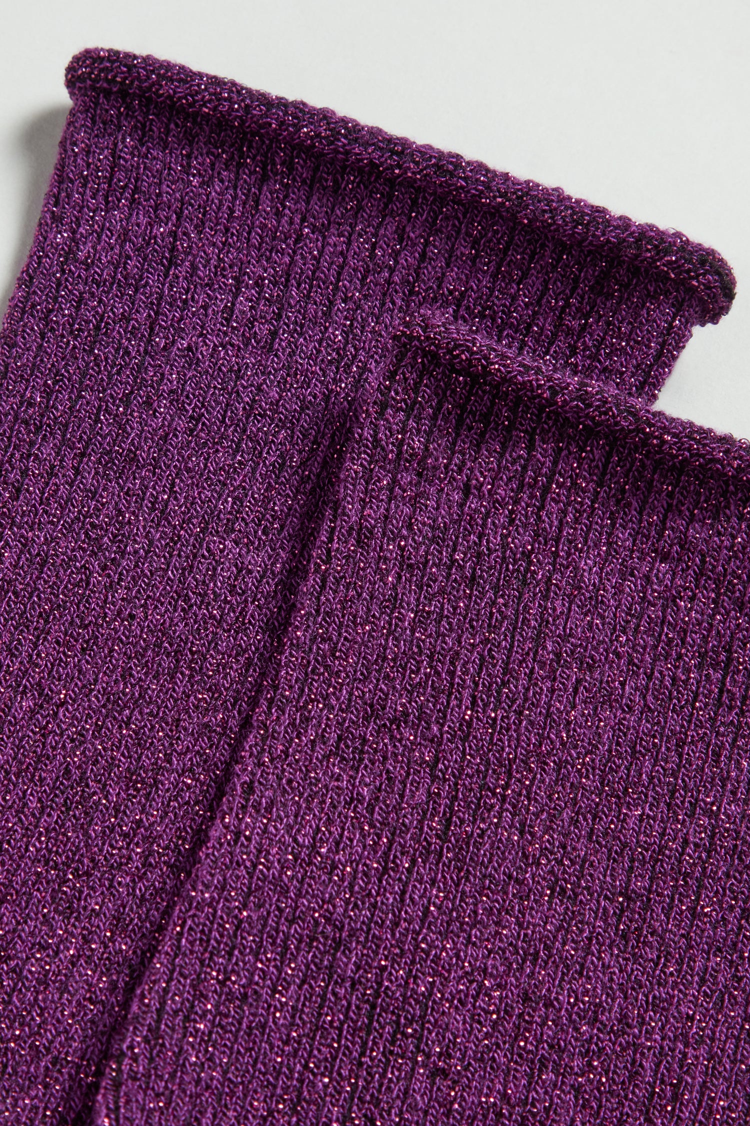 Close-up of two ribbed, glittery purple fabric pieces from Bamboo Sparkle Purple Socks, laid flat on a surface.