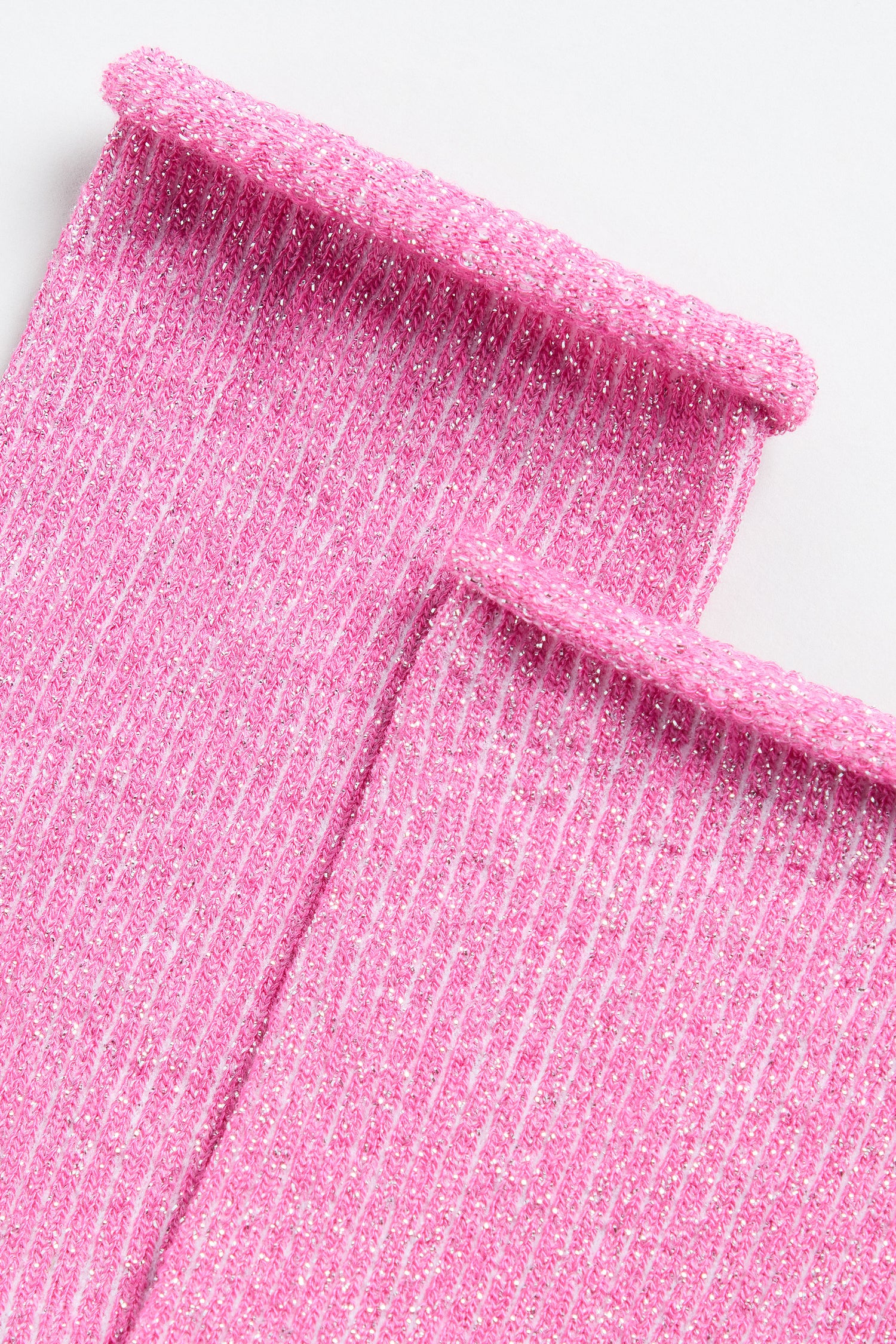 Close-up of two Bamboo Sparkle Fuchsia Socks with pink, ribbed, glittery fabric and rolled edges, laid side by side on a white background.