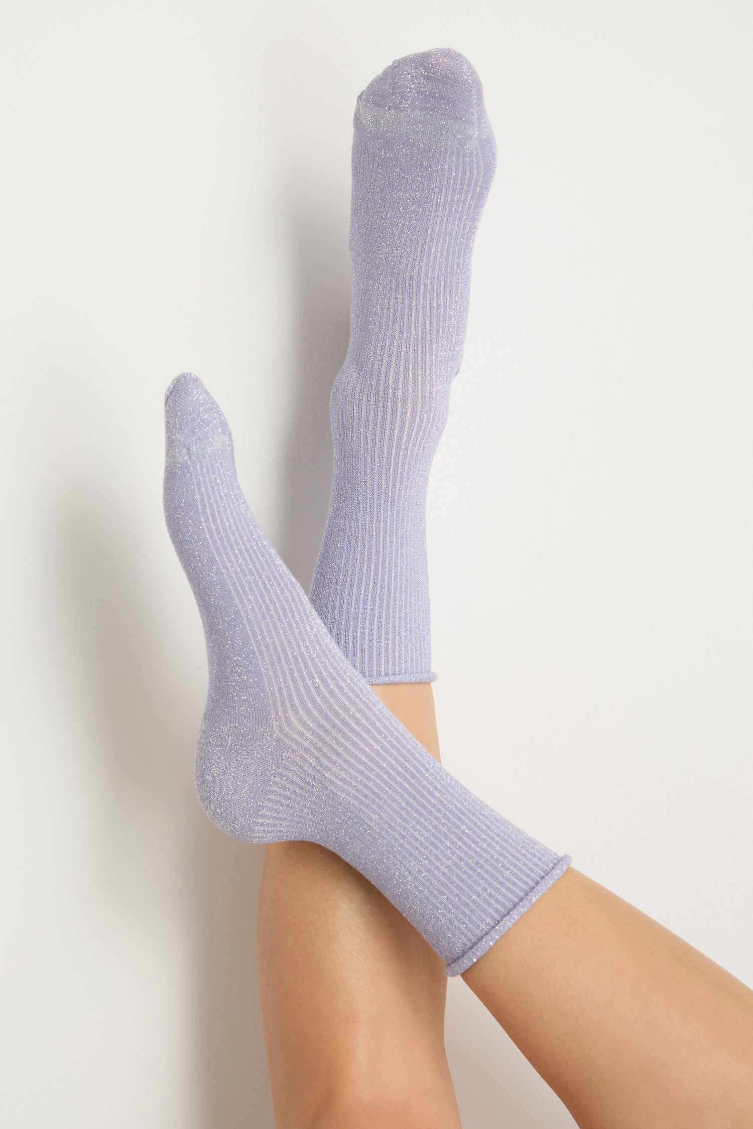 A person with crossed legs is wearing Bamboo Sparkle Lilac Socks against a plain white background.