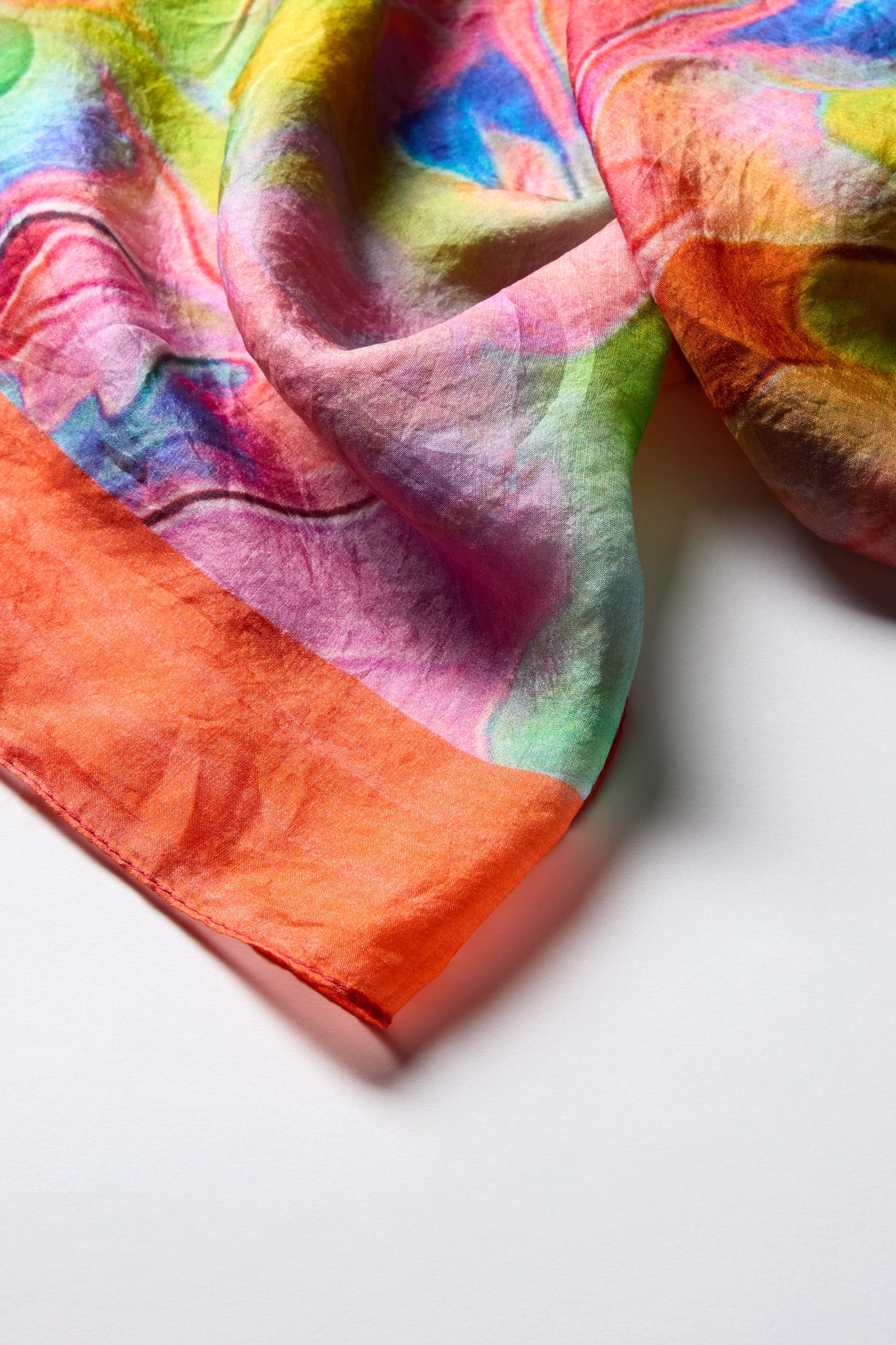 A luxurious Tiffany Lamp Silk Scarf with swirling patterns of pink, orange, green, and blue elegantly drapes over a white surface.