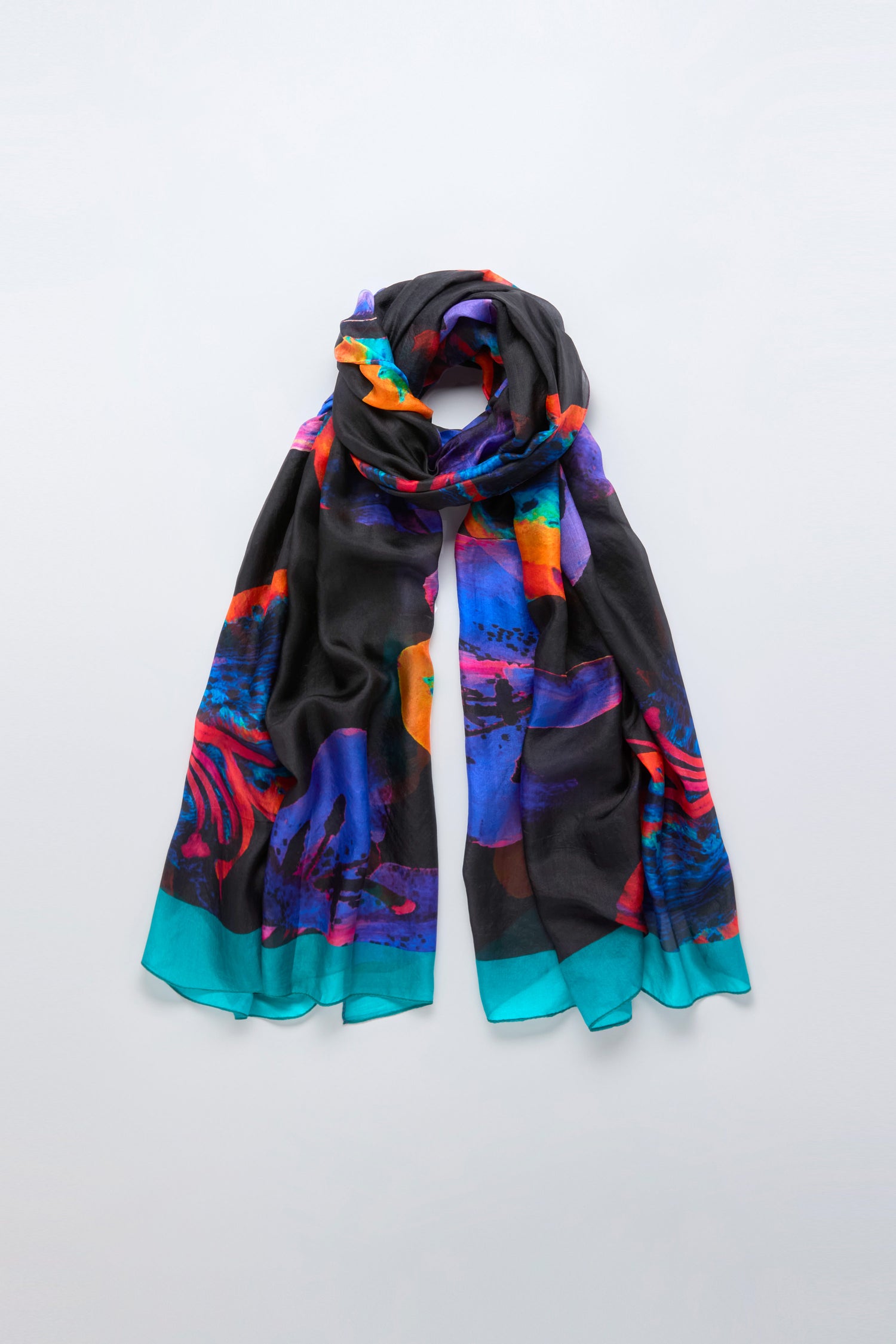 The Orchid Silk Scarf is a long, lightweight accessory featuring a vibrant abstract pattern in blue, purple, orange, and teal tones, shown folded against a light background for a modern elegant look.