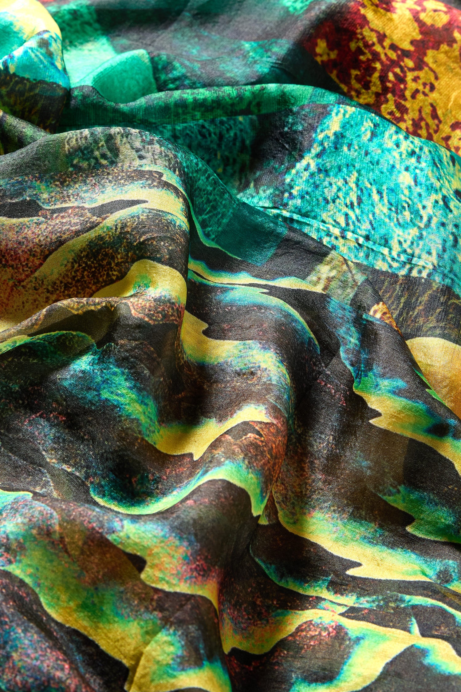Close-up of crumpled fabric features the Northern Lights Silk Scarf—a luxurious accessory with a vibrant, abstract design in green, yellow, black, and red tones.