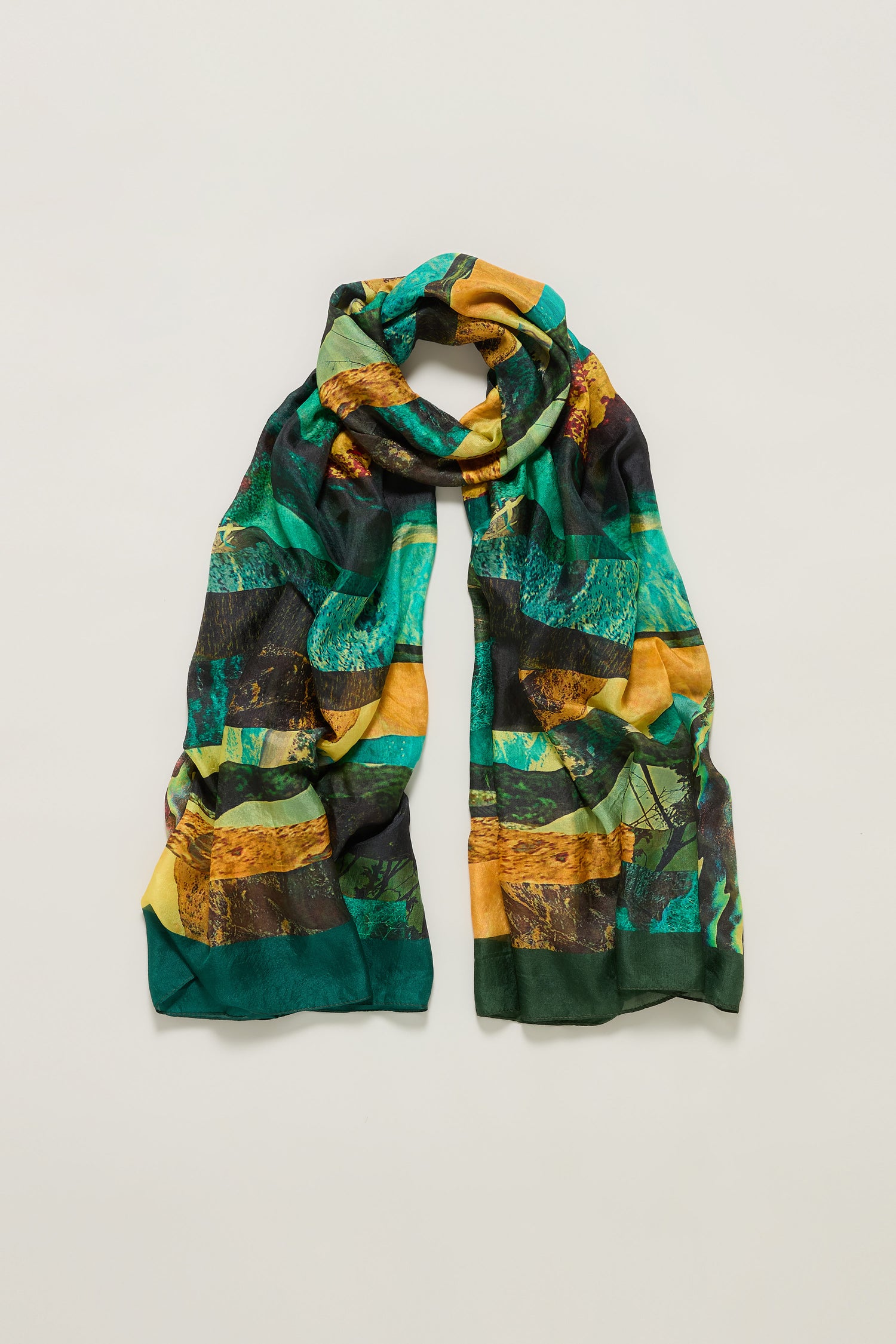 The Northern Lights Silk Scarf is a lightweight accessory featuring an abstract design in green, yellow, and black tones, shown laid flat on a neutral background for a touch of luxury.