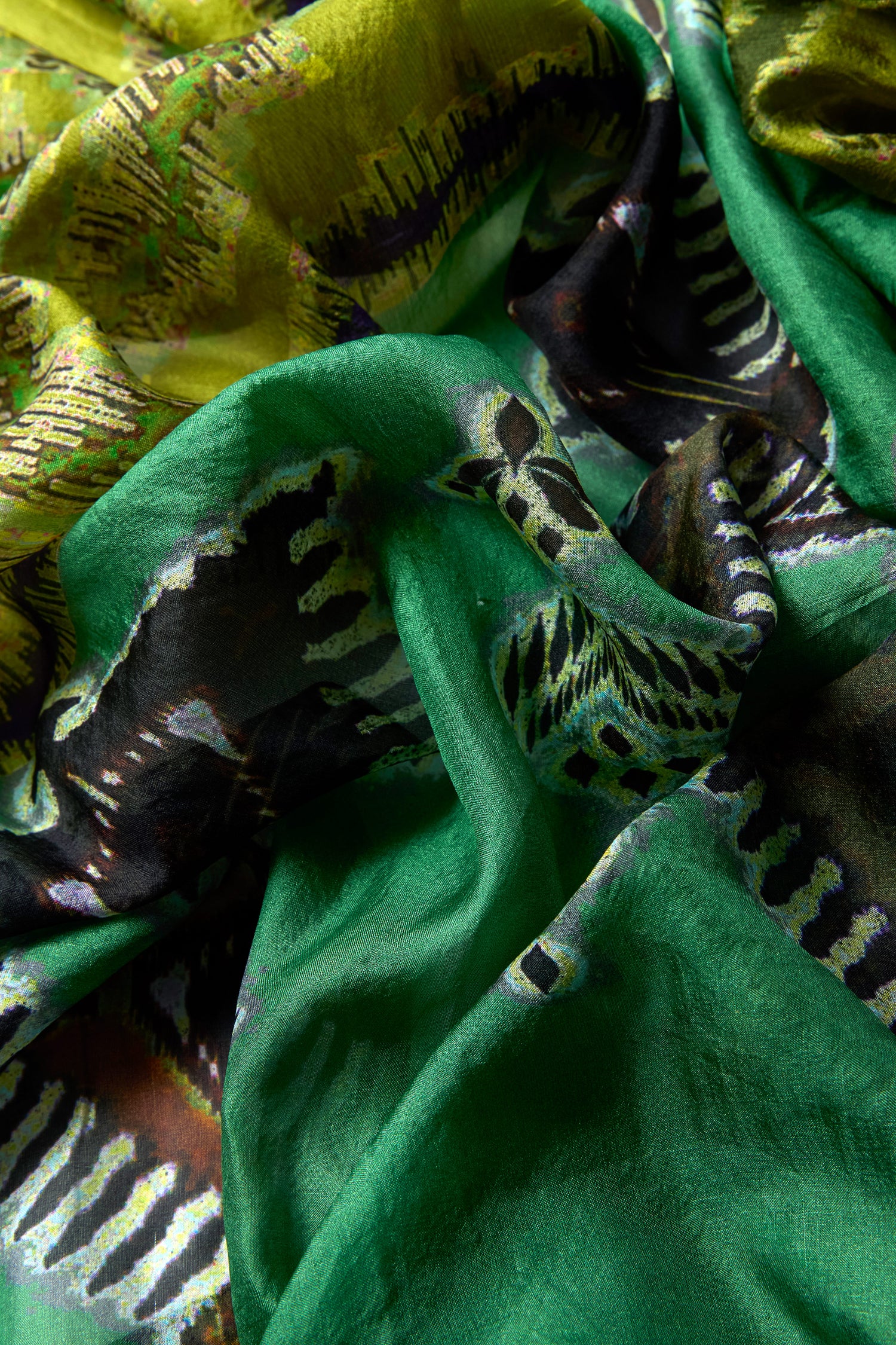 Close-up of the Aztec Silk Scarf, featuring crumpled green and yellow patterns with black and white abstract designs.