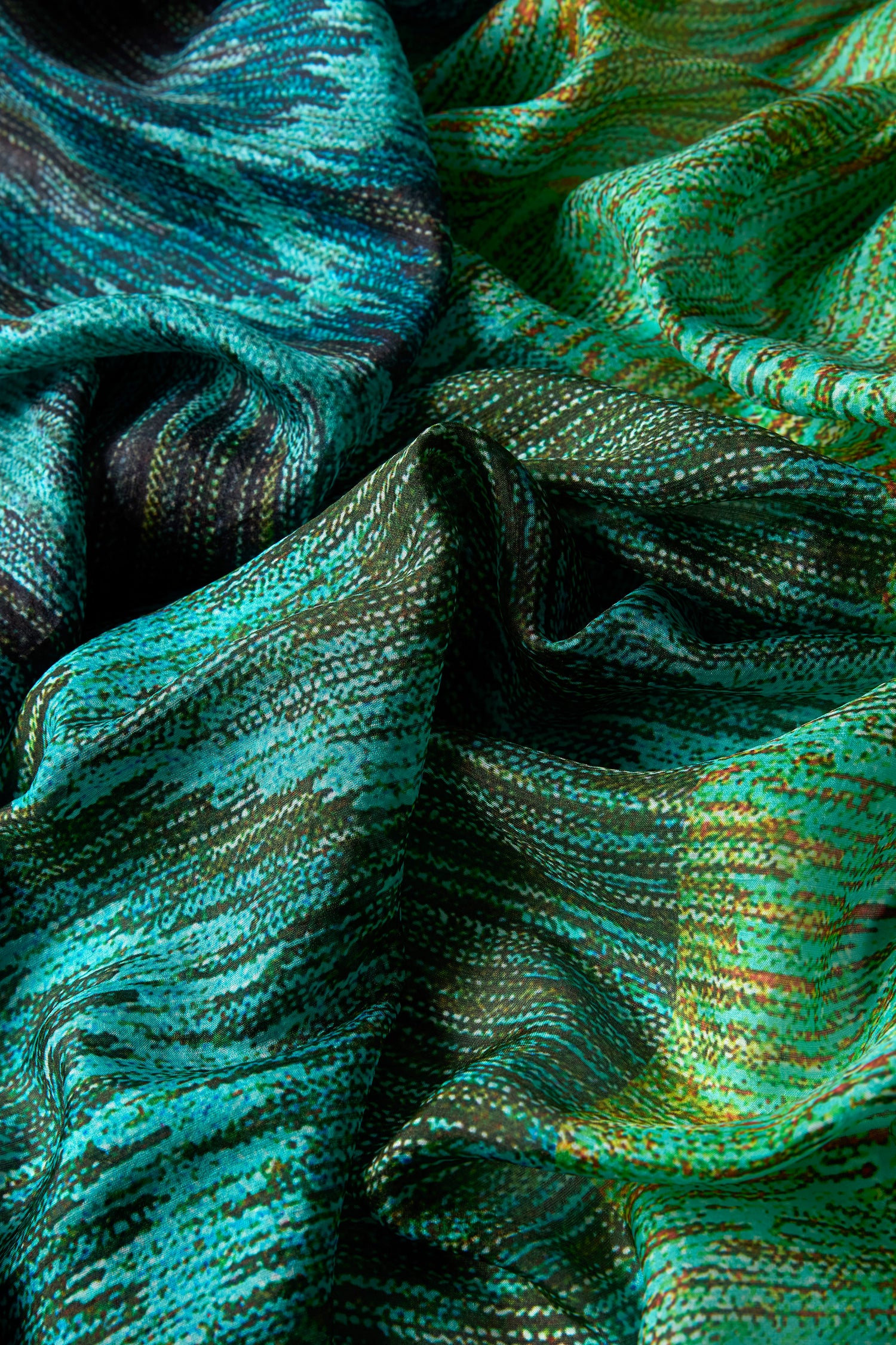 Close-up of the Shaded Sketch Green and Blue Silk Scarf, featuring lightweight textured silk with wavy abstract patterns and streaks in green, turquoise, and blue, highlighting the elegant folds.