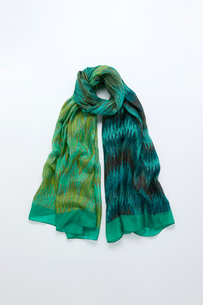 The Shaded Sketch Green and Blue Silk Scarf, featuring an abstract print, is laid flat on a light background with both ends spread out and a loop at the top.