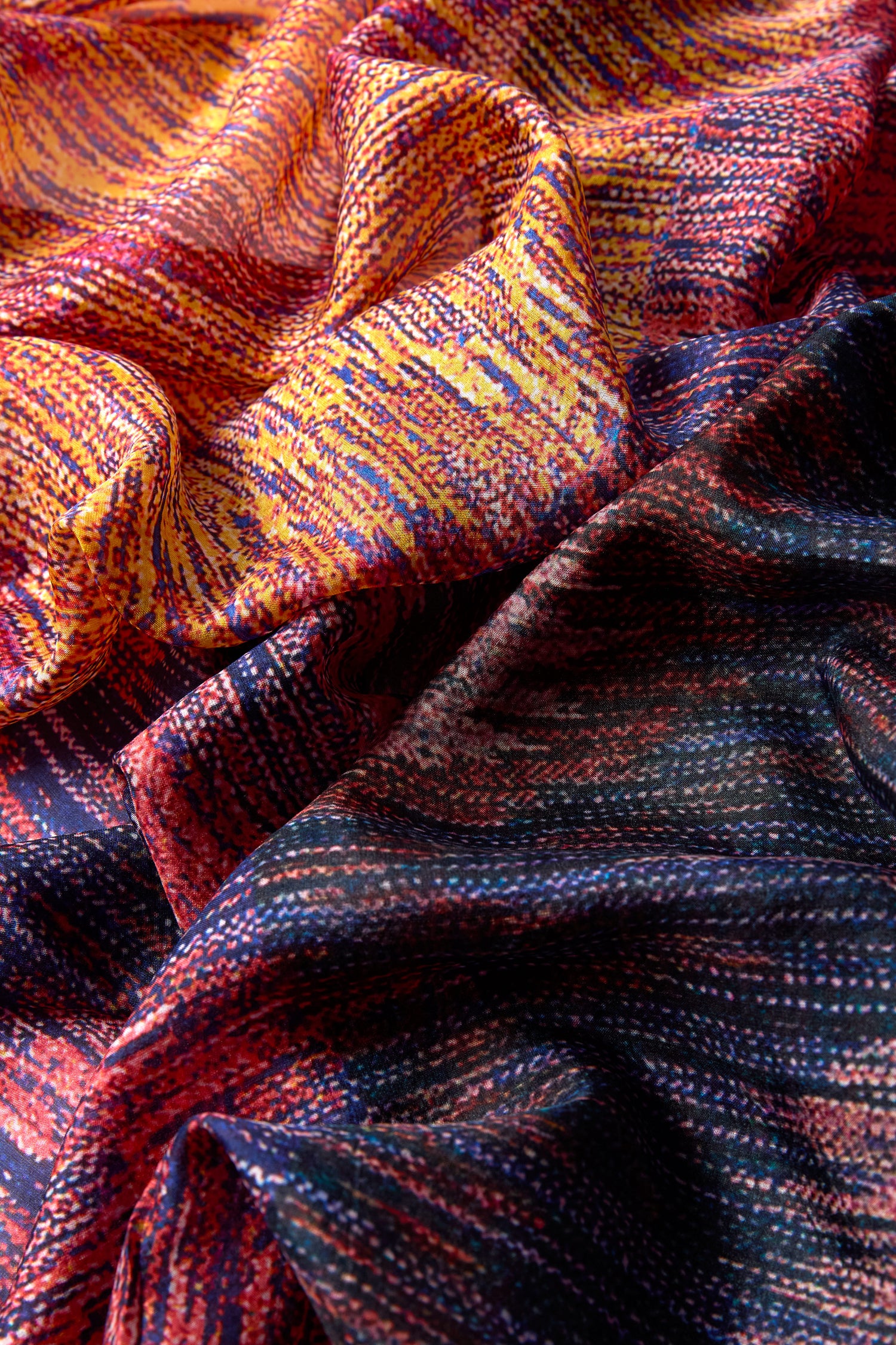 Close-up of the Shaded Sketch Silk Scarf, featuring colorful folds and textured woven patterns in yellow, orange, purple, and blue hues.