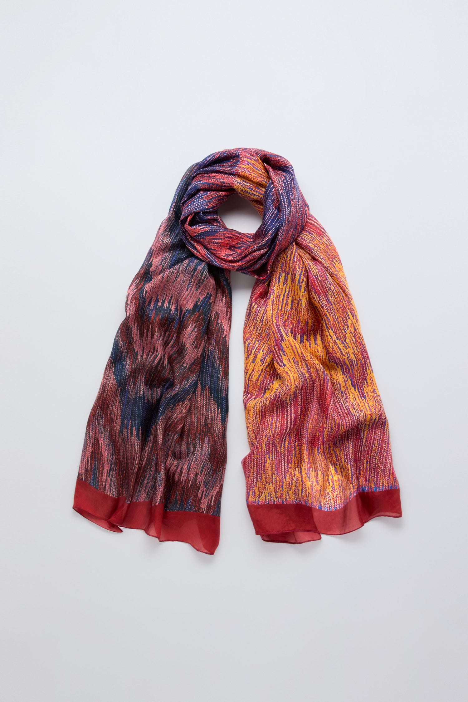 The Shaded Sketch Silk Scarf features a multicolored brushstroke print in red, blue, and yellow with bold red borders, displayed flat with its ends elegantly draped down.