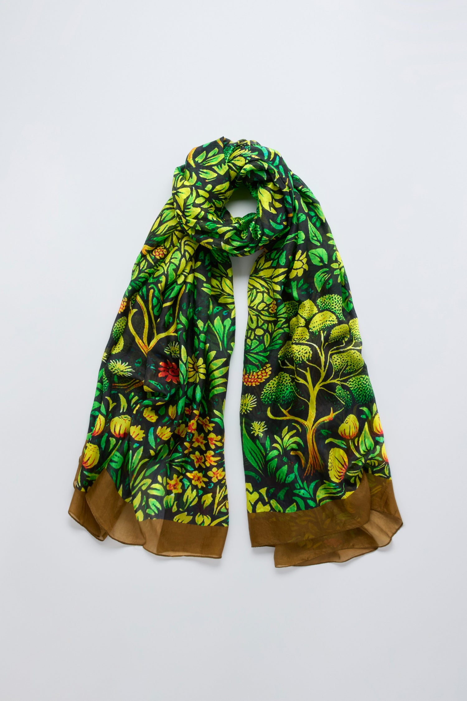The Autumnal Garden Silk Scarf features a green, yellow, and brown botanical pattern of trees and leaves, evoking autumn foliage, displayed against a plain background.