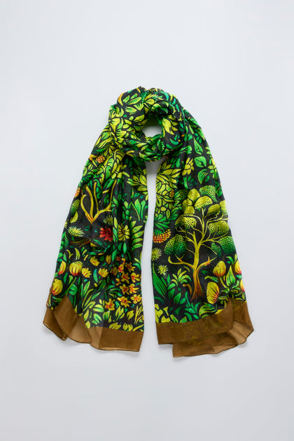 The Autumnal Garden Silk Scarf features a green, yellow, and brown botanical pattern of trees and leaves, evoking autumn foliage, displayed against a plain background.