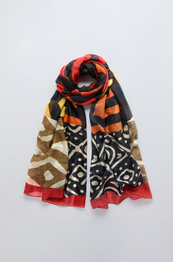 The Ancient Silk Scarf showcases black, yellow, brown, and red tribal-inspired prints in a modern design, displayed flat on a light gray background.