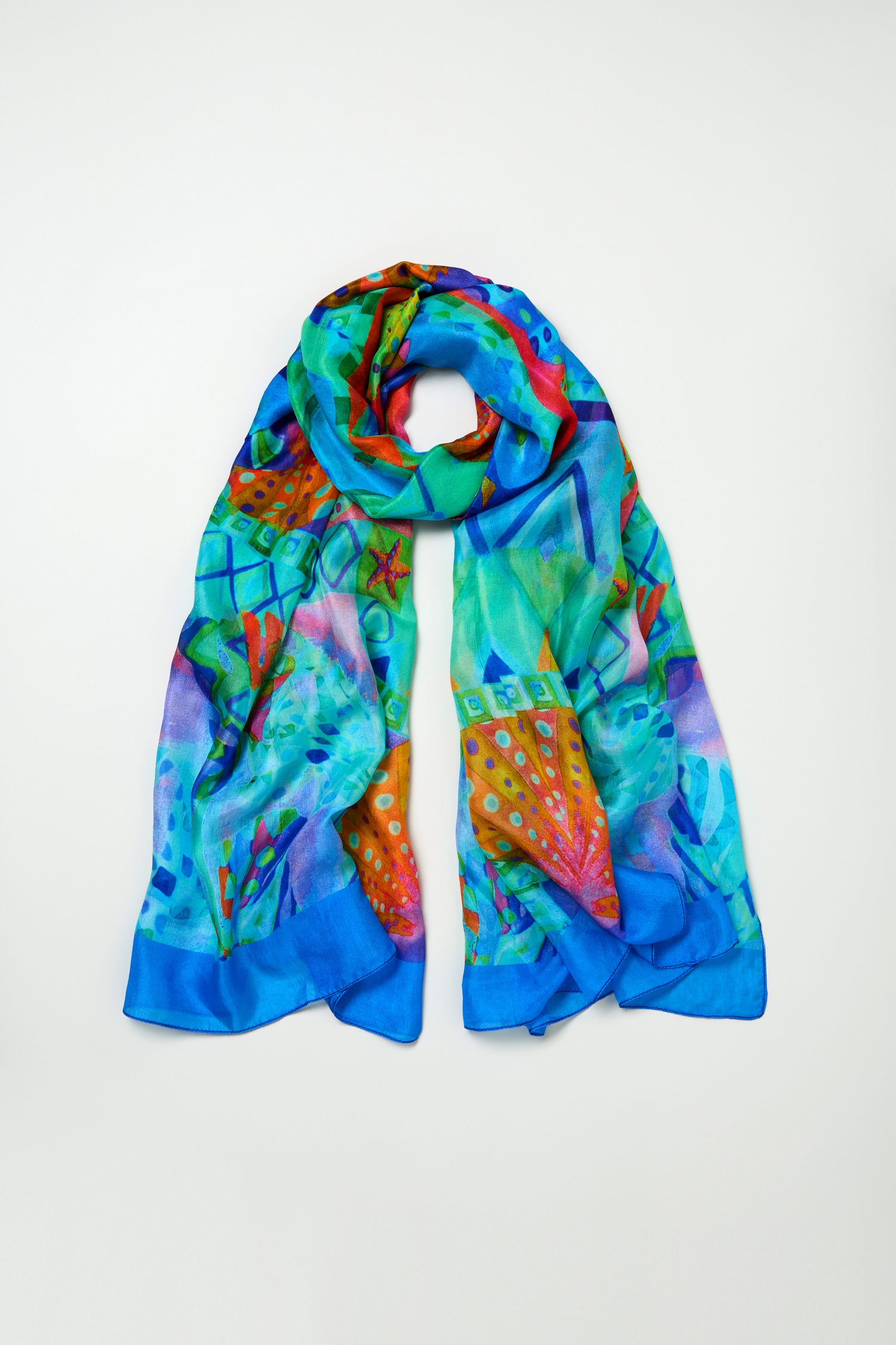 The Ocean Garden Silk Scarf, with a luxurious sheen and vibrant abstract patterns in blue, green, orange, and red tones, is displayed flat on a plain light background.