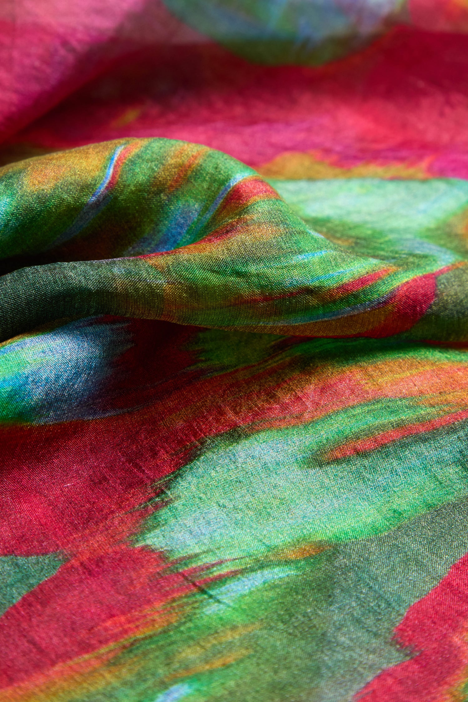 Close-up of the Blurred Botanicals Scarf: luxe, brightly colored tie-dye fabric with vibrant red, green, blue, and yellow patterns, reminiscent of bold florals with visible texture.