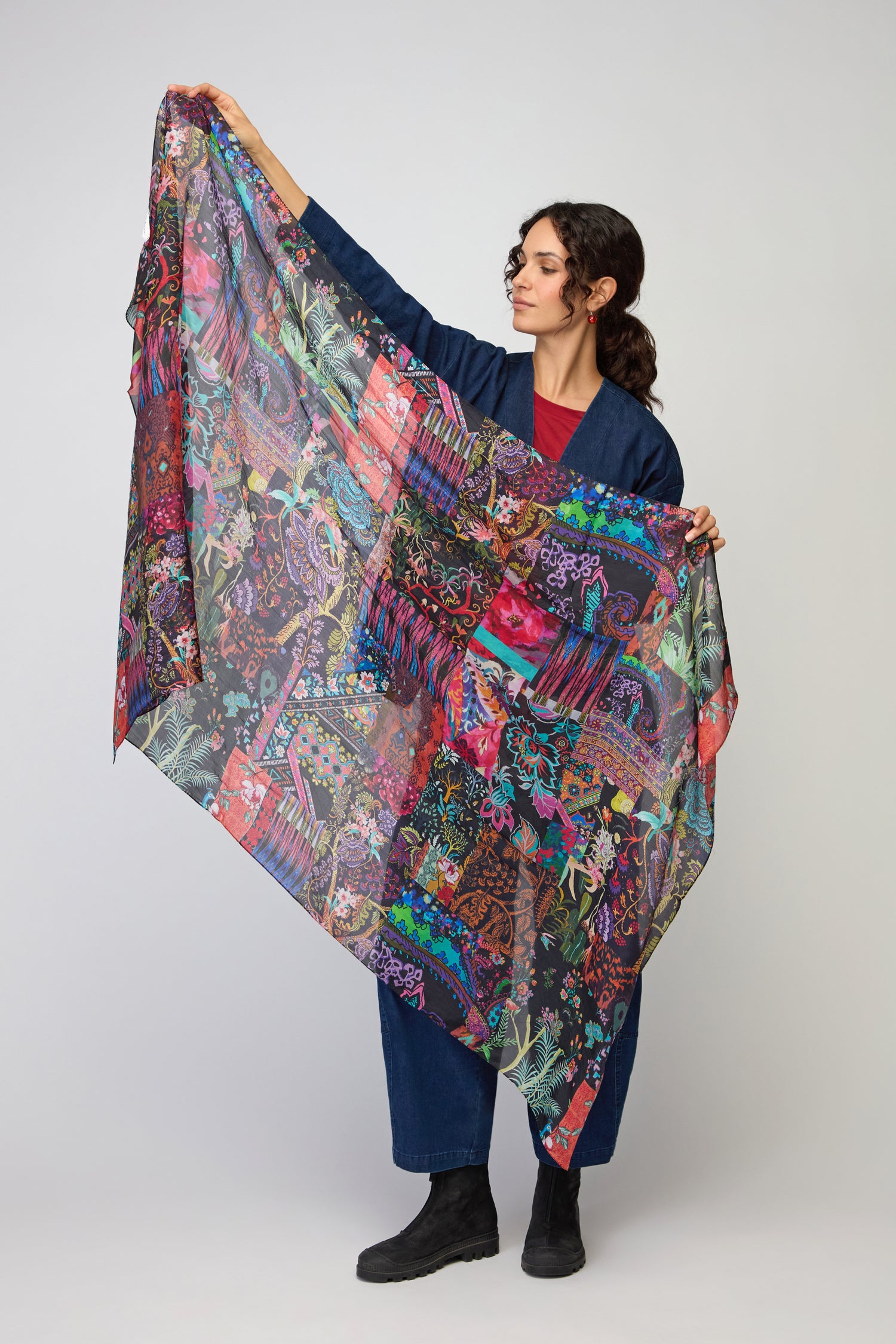 A woman in dark clothing displays the Sahara Winter Patchwork Scarf, featuring vibrant colors, against a plain light background.