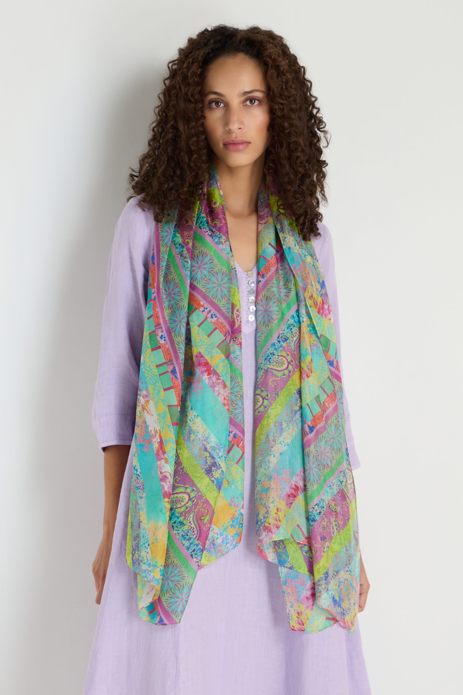 A woman wearing a light purple dress and the Archival Stripe Silk Scarf stands against a plain light background.