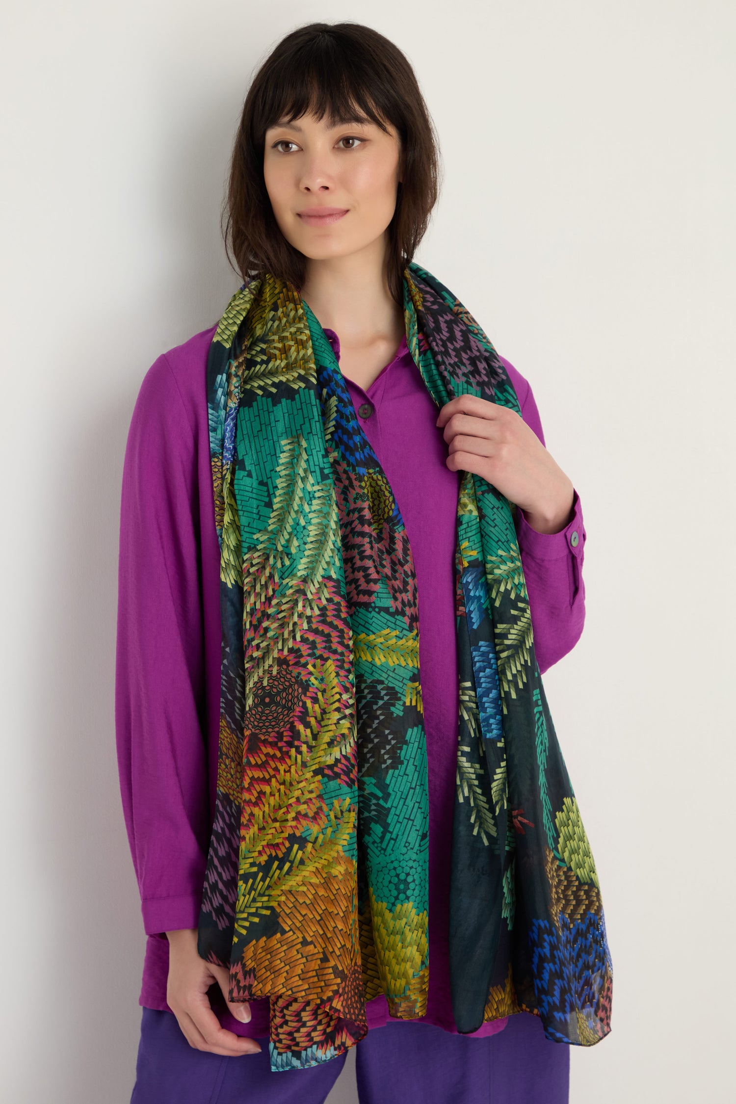 Woman wearing a loose purple top and pants, with the Pixelated Petals Silk Scarf draped around her neck, standing against a plain light background.