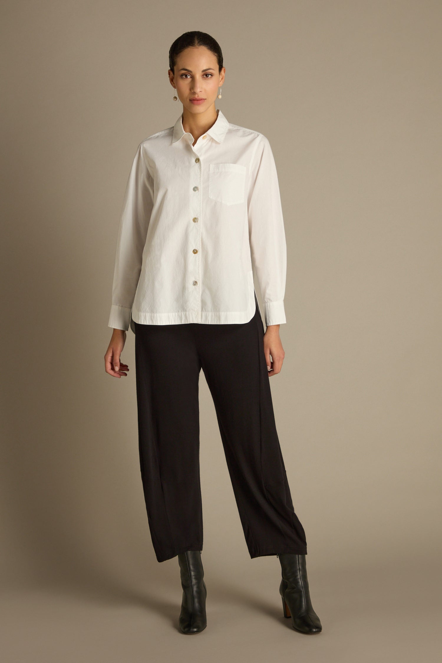 A person wearing the Curved Hem Shirt, a premium cotton button-up in white, along with black pants stands against a plain background.