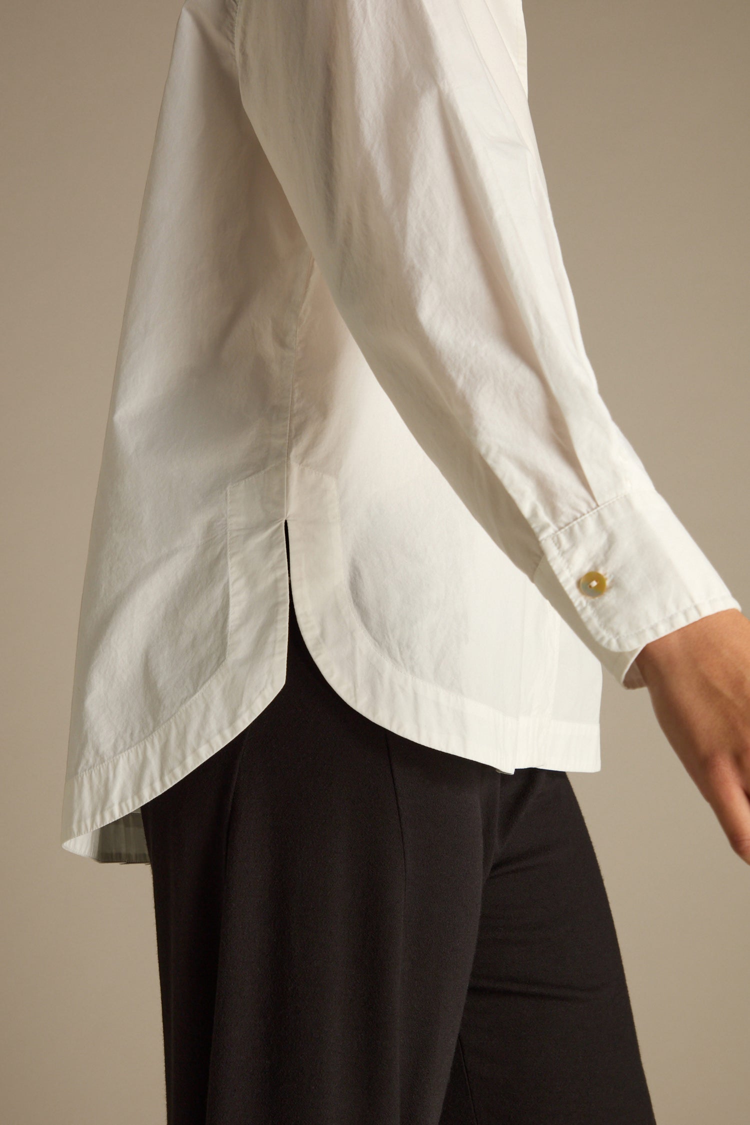 A person wearing a Curved Hem Shirt in premium cotton white with long sleeves and black pants stands against a neutral background.