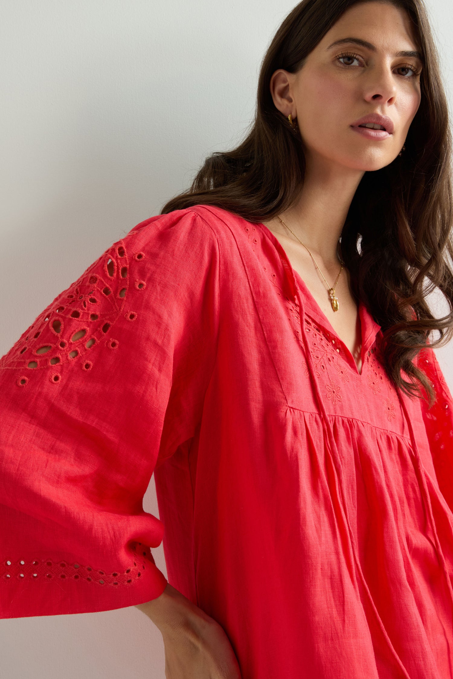 A woman wears the Embroidered Schiffli Linen Top, featuring a loose fit, bright red color, eyelet details, and delicate embroidery, standing against a plain light background.