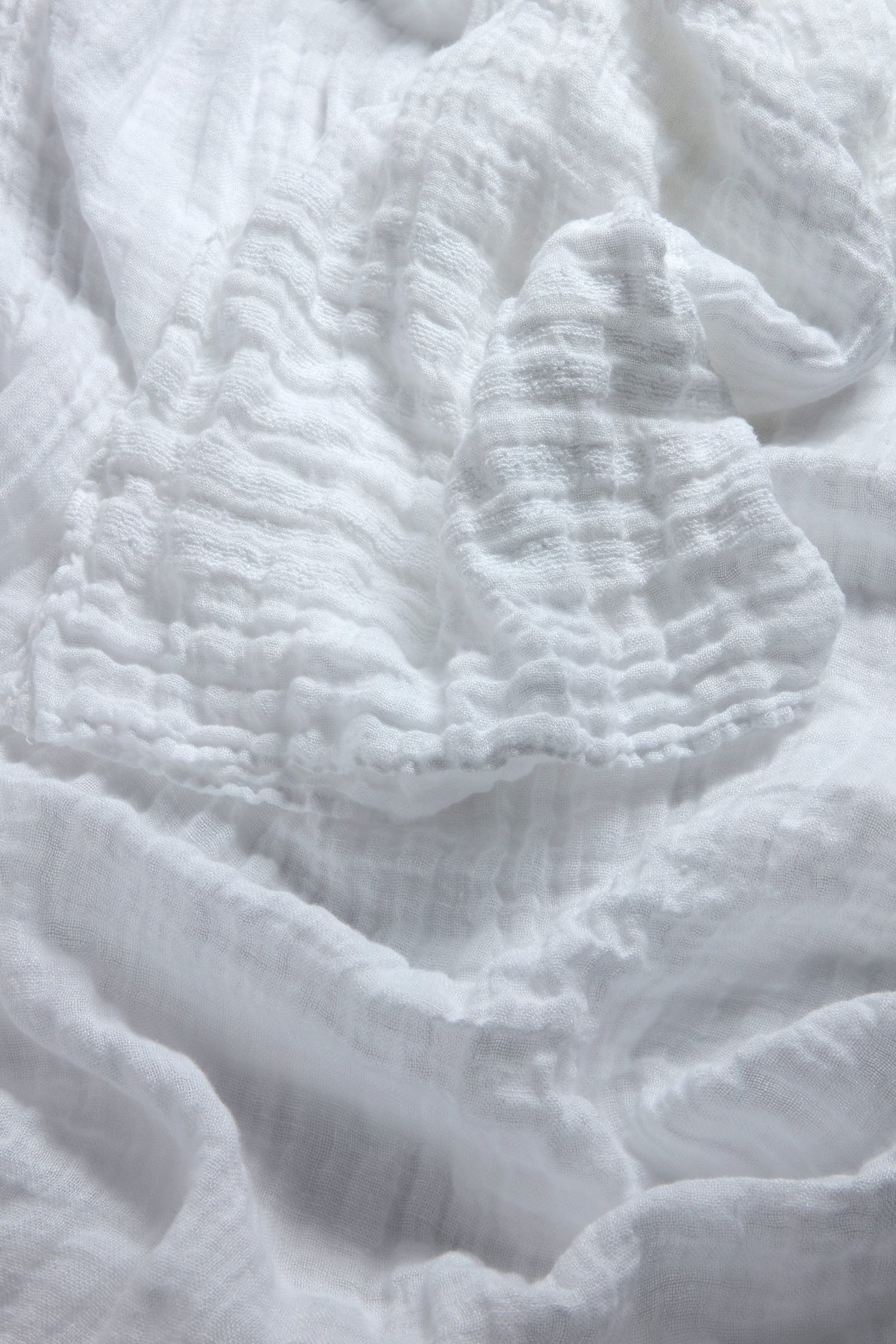 A close-up of soft, crumpled white fabric with a wavy texture, reminiscent of the versatile Crinkle Linen Scarf.