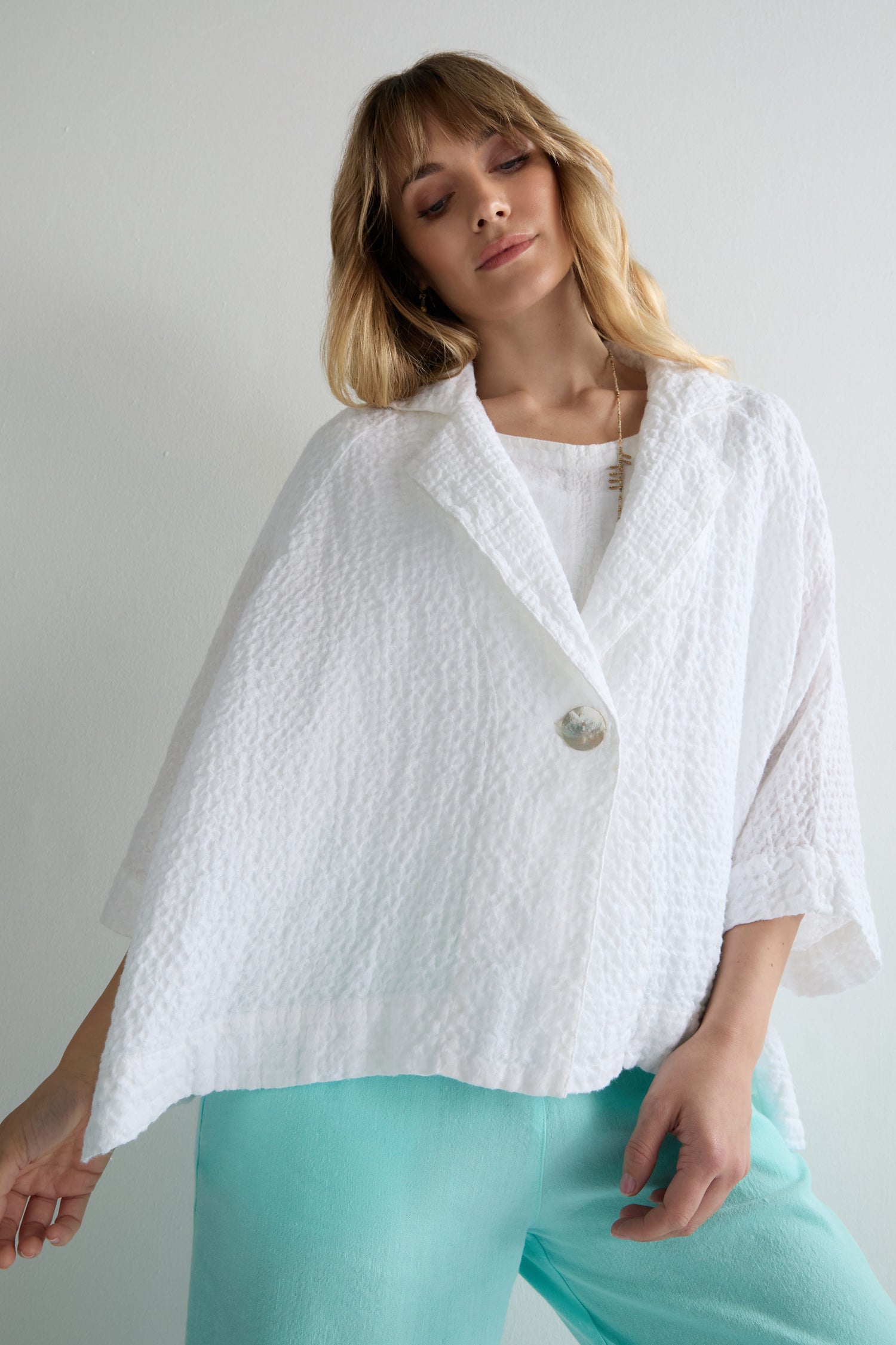 Woman wearing the Garment Dyed Waffle Linen Boxy Jacket, a textured white button-up, layered over a white top and light blue pants, standing against a plain light background.