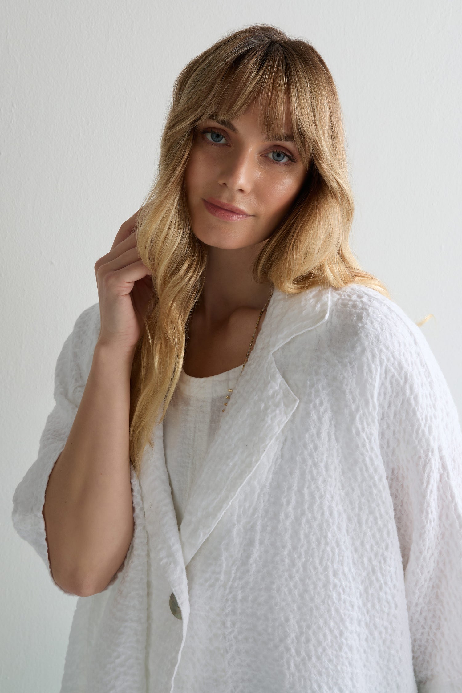 A woman with long blonde hair wears a Garment Dyed Waffle Linen Boxy Jacket in white, styled oversized and paired with a matching top, standing against a plain light-colored wall.