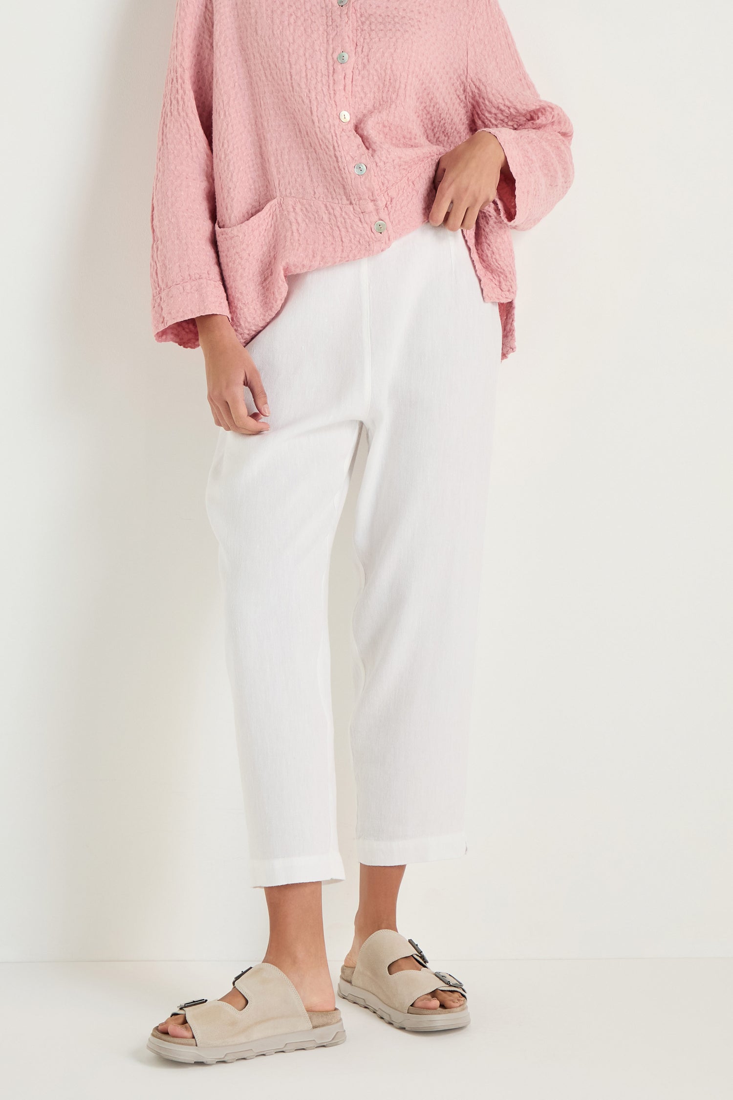 Person wearing a textured pink button-up top, beige slide sandals, and Twisted Linen Slim White Trouser, standing against a plain white background.
