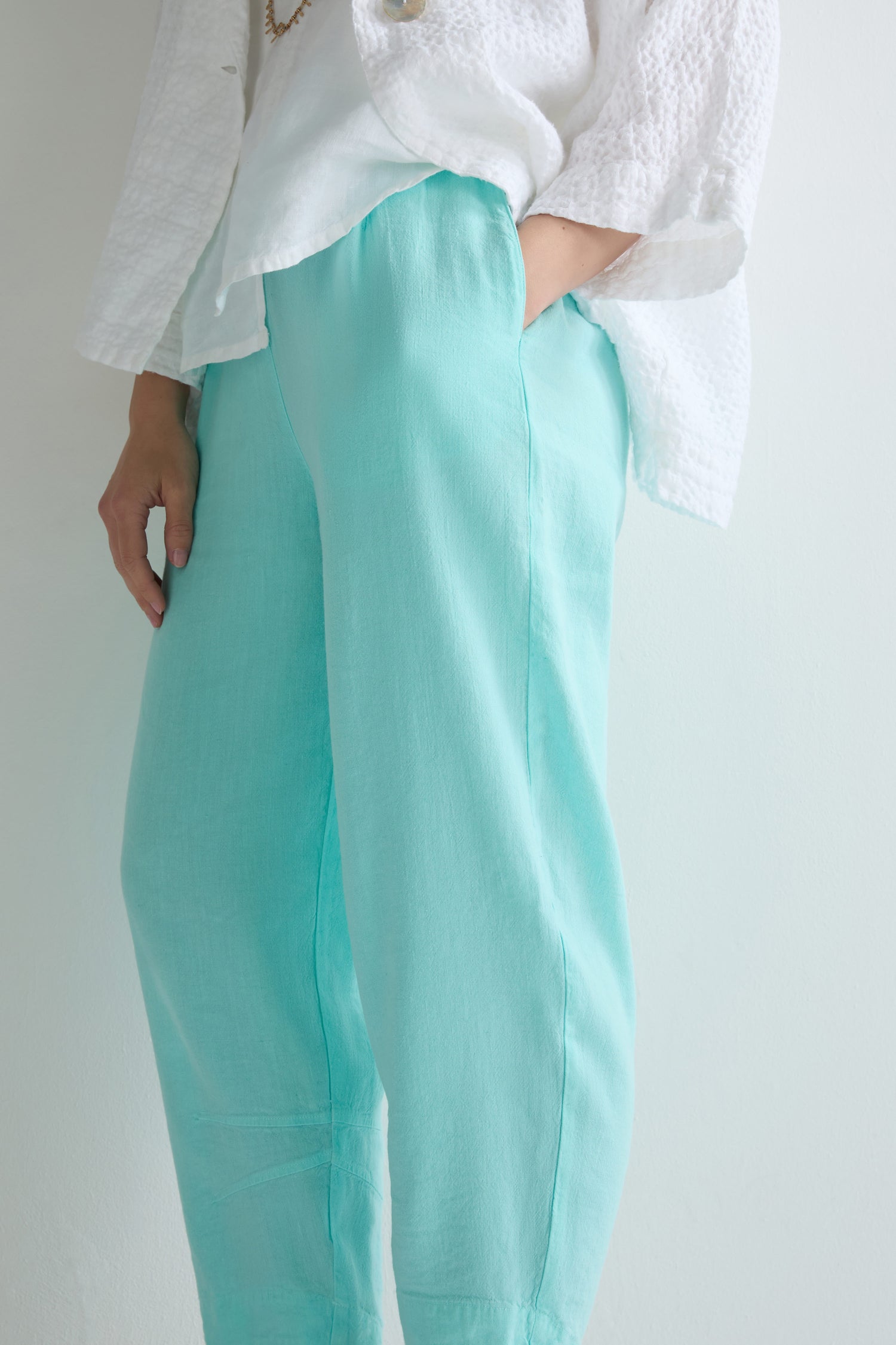 Person wearing Mint Twisted Linen Crop Bubble Trouser in a bubble shape, light blue, paired with a white textured long-sleeve top with one hand in their pocket, standing against a light background.