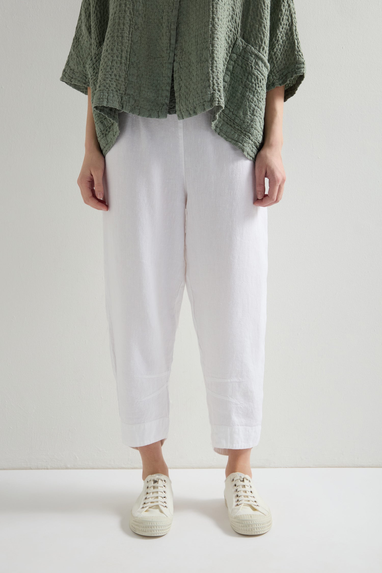 A person in a textured green top, Twisted Linen Crop Bubble Trouser with an elastic waistband, and white sneakers stands against a plain background.