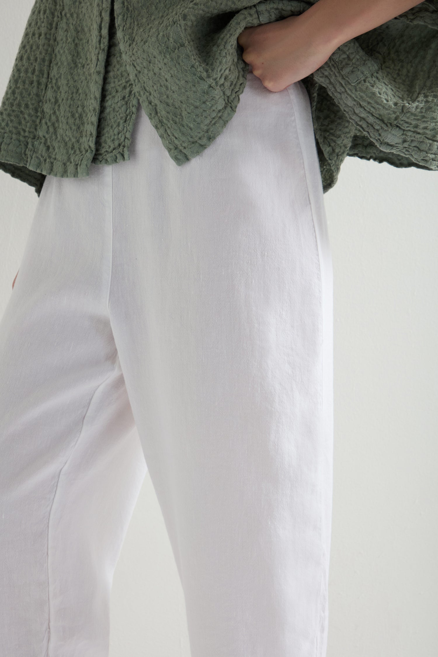 Dressed in a textured green top and Twisted Linen Crop Bubble Trouser, the individual gives off a laid-back vibe, standing with one hand in their pants pocket.