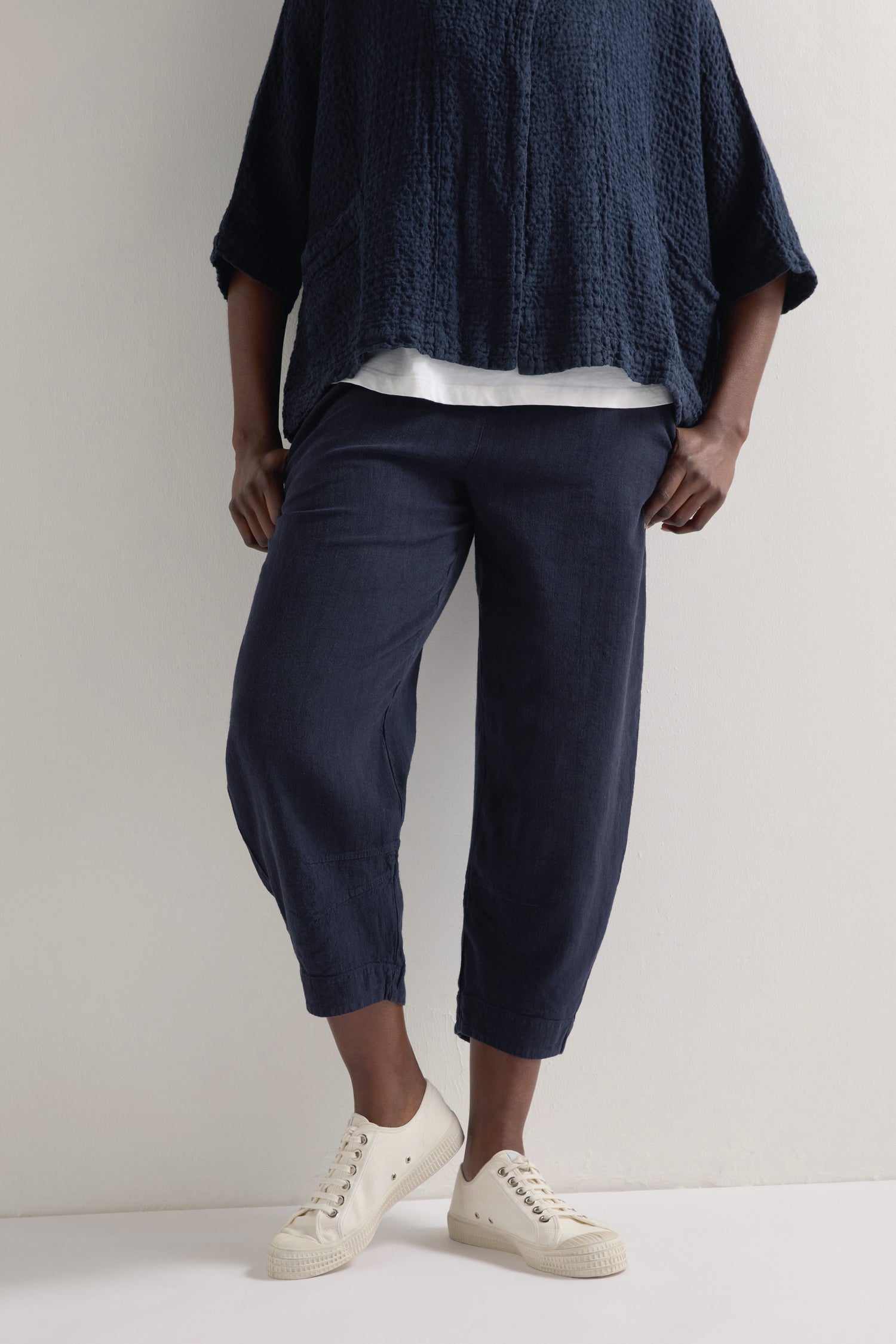 A person in a textured navy top and wide Twisted Linen Crop Bubble Trouser with an elasticated waistband, teamed with white sneakers, is set against a plain background.