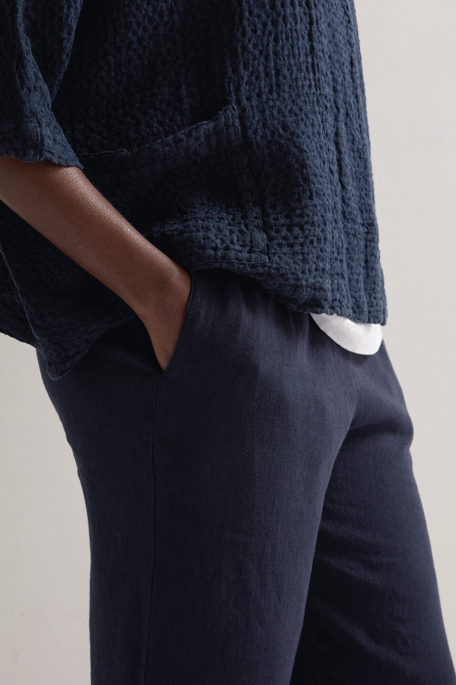 A person in a textured navy top and Twisted Linen Crop Bubble Trousers with an elasticated waistband stands with hands in pockets against a light background, exuding effortless style through the cropped bubble silhouette.