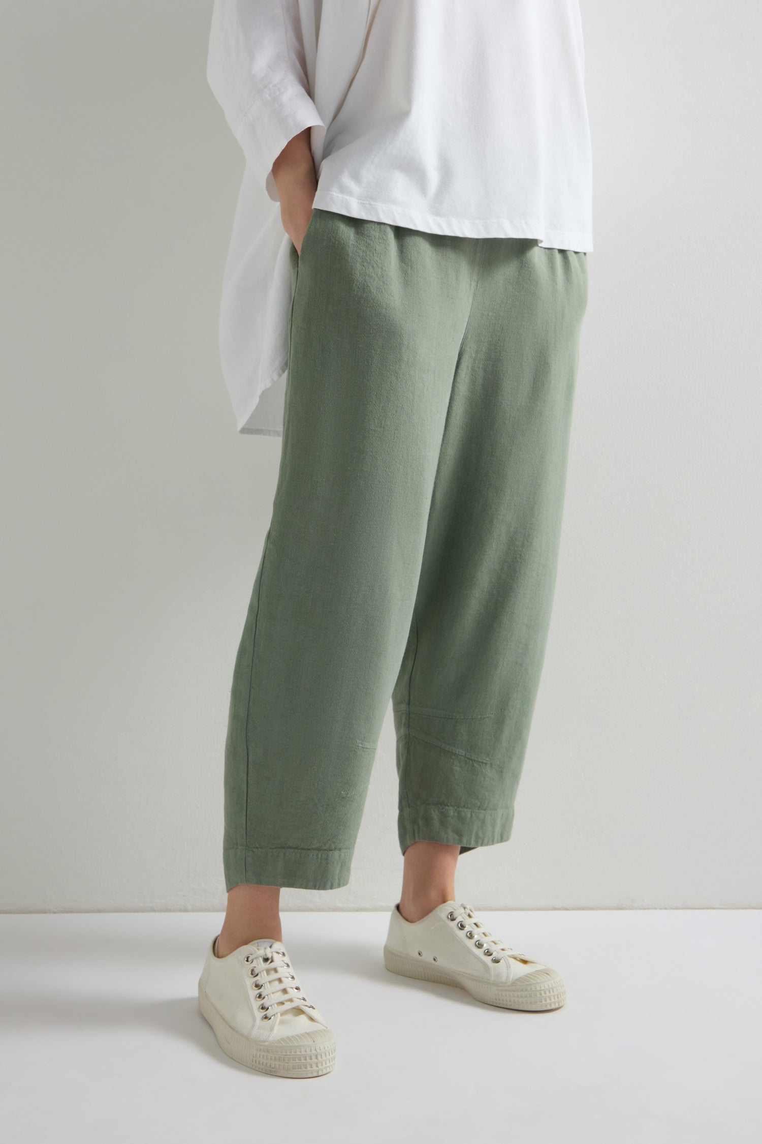 Person in a white shirt and white sneakers wears the Twisted Linen Crop Bubble Trouser, featuring an elastic waistband, standing with hands in pockets.