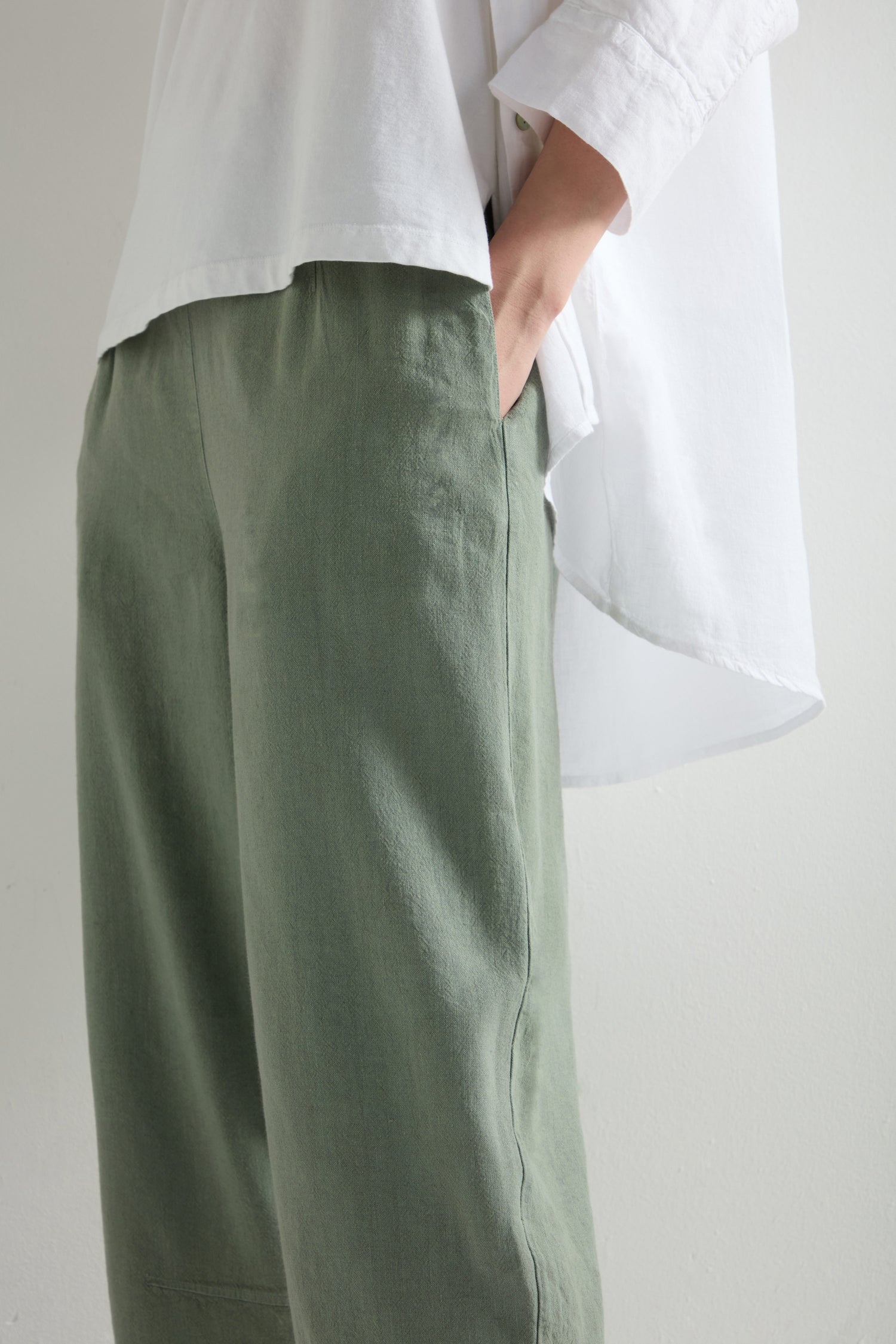 A person in a white shirt wearing stylish green Twisted Linen Crop Bubble Trousers with an elastic waistband, stands with one hand in their pocket.