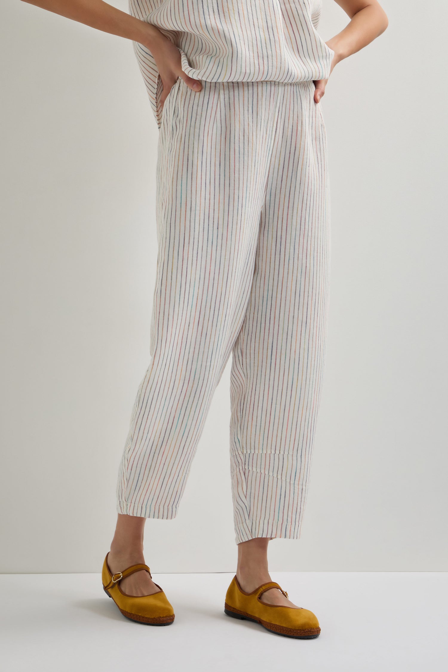 A person stands against a plain background wearing White Space Dye Stripe Bubble Trousers paired with yellow Mary Jane shoes.